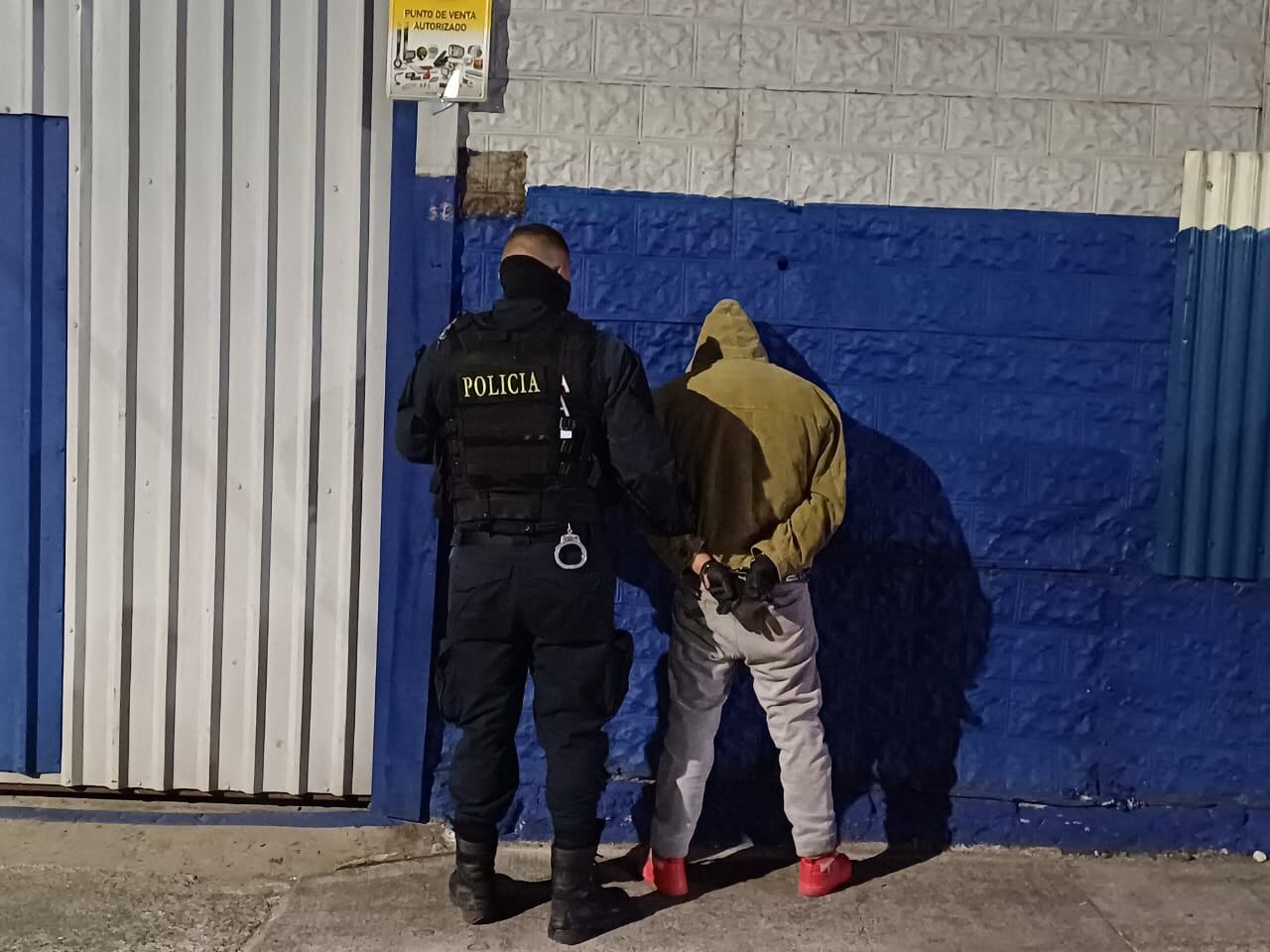 Dos hombres de espaldas, uno es un policía que está capturando al otro.