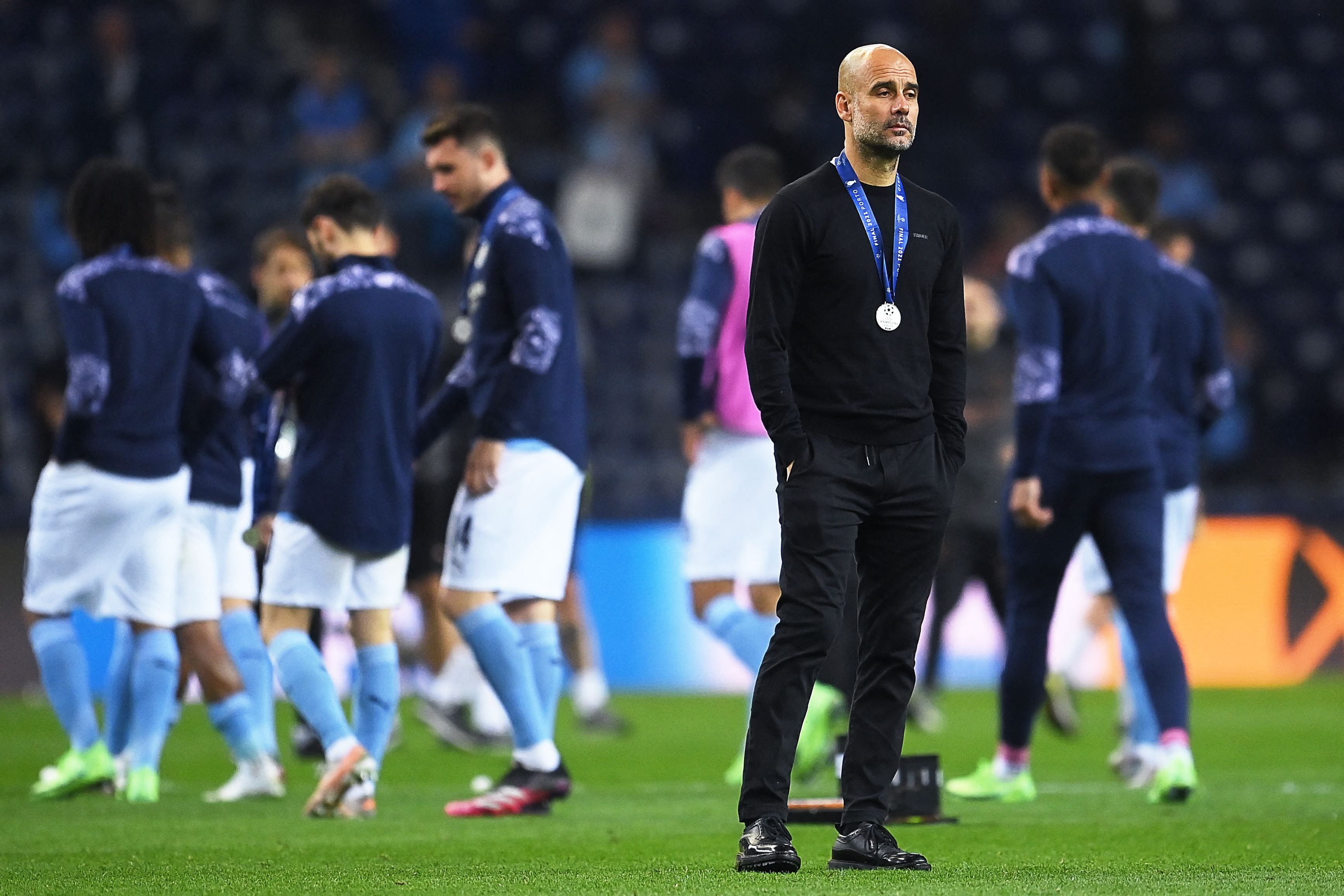 Imagen del entrenador de fútbol Joseph Guardiola en lo que parece el final de un partido. Se le ve con una medalla en su cuello, ropa deportiva de color negro.