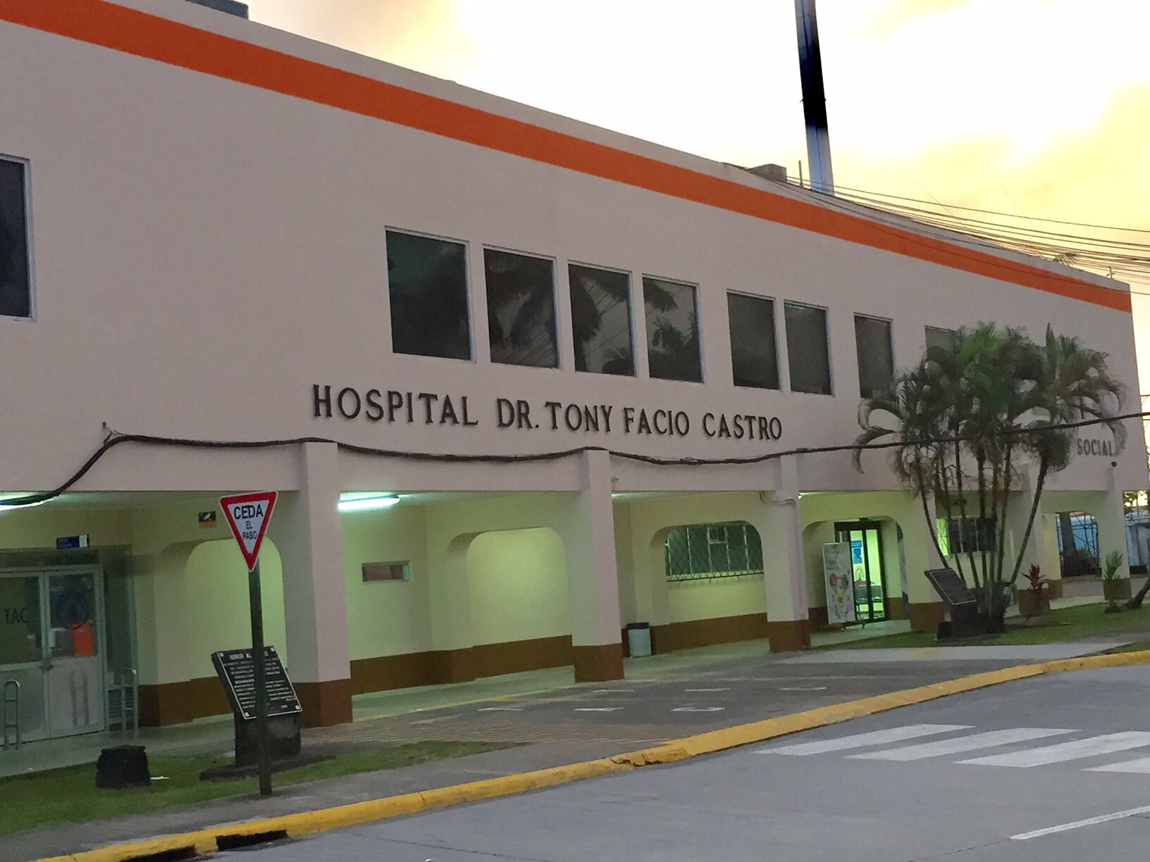 Fachada de un edificio de una planta, de color crema con bordes anaranjados. Con letrero negro que dice Hospital Dr. Tony Facio Castro