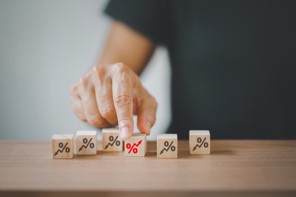 Una mano selecciona un bloque de madera con un ícono de porcentaje y una flecha roja hacia arriba, representando el aumento de los riesgos asociados con los créditos de consumo a largo plazo en las cooperativas financieras.