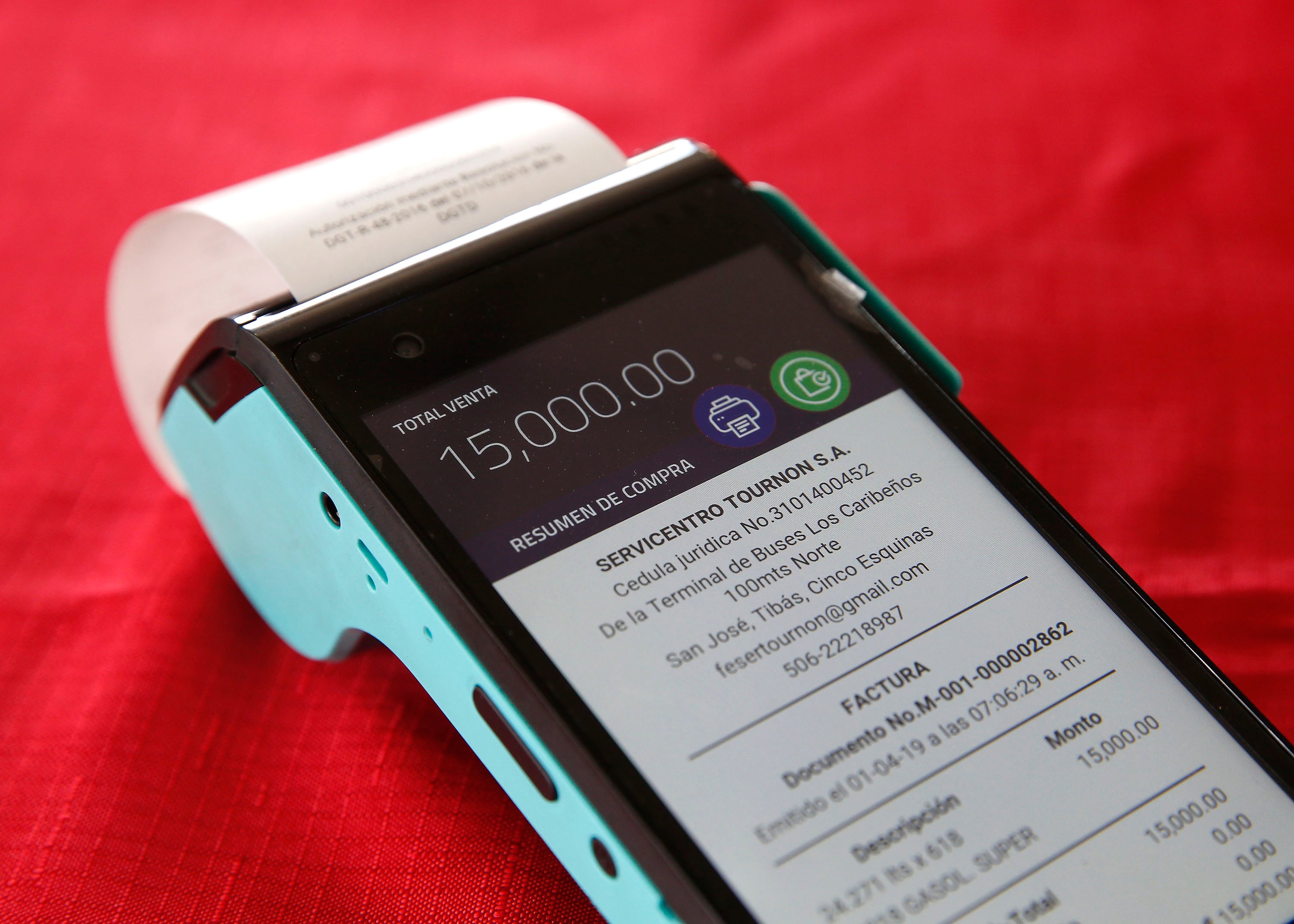Dispositivo para emitir facturas electrónicas en una gasolinera, mostrando el detalle de la transacción sobre un fondo rojo.