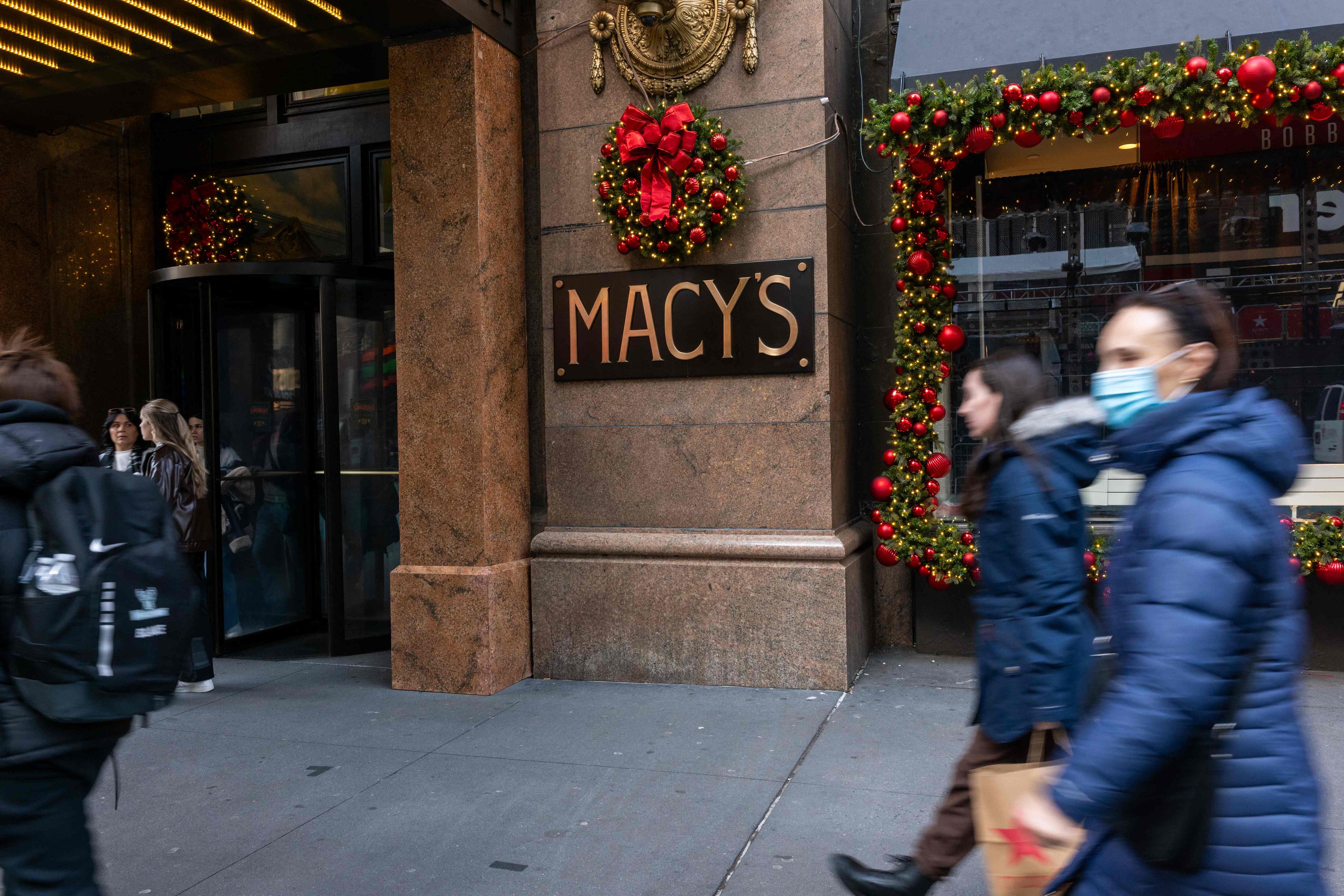 Vista de la entrada principal de Macy’s en Nueva York decorada con guirnaldas y adornos navideños. Varias personas caminan frente a la tienda.