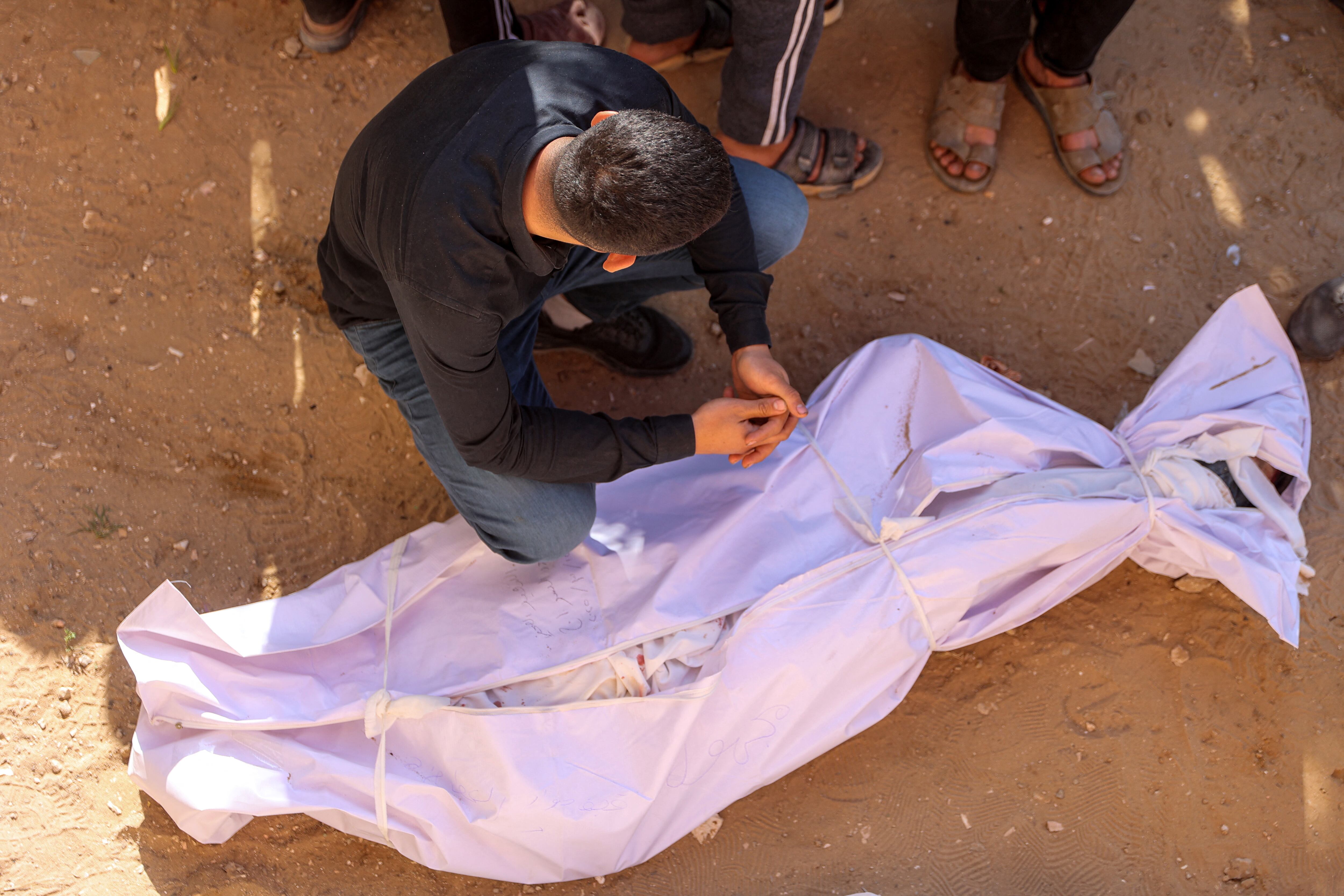 Hombre llora frente a cuerpo de familiar muerto envuelto en manta blanca