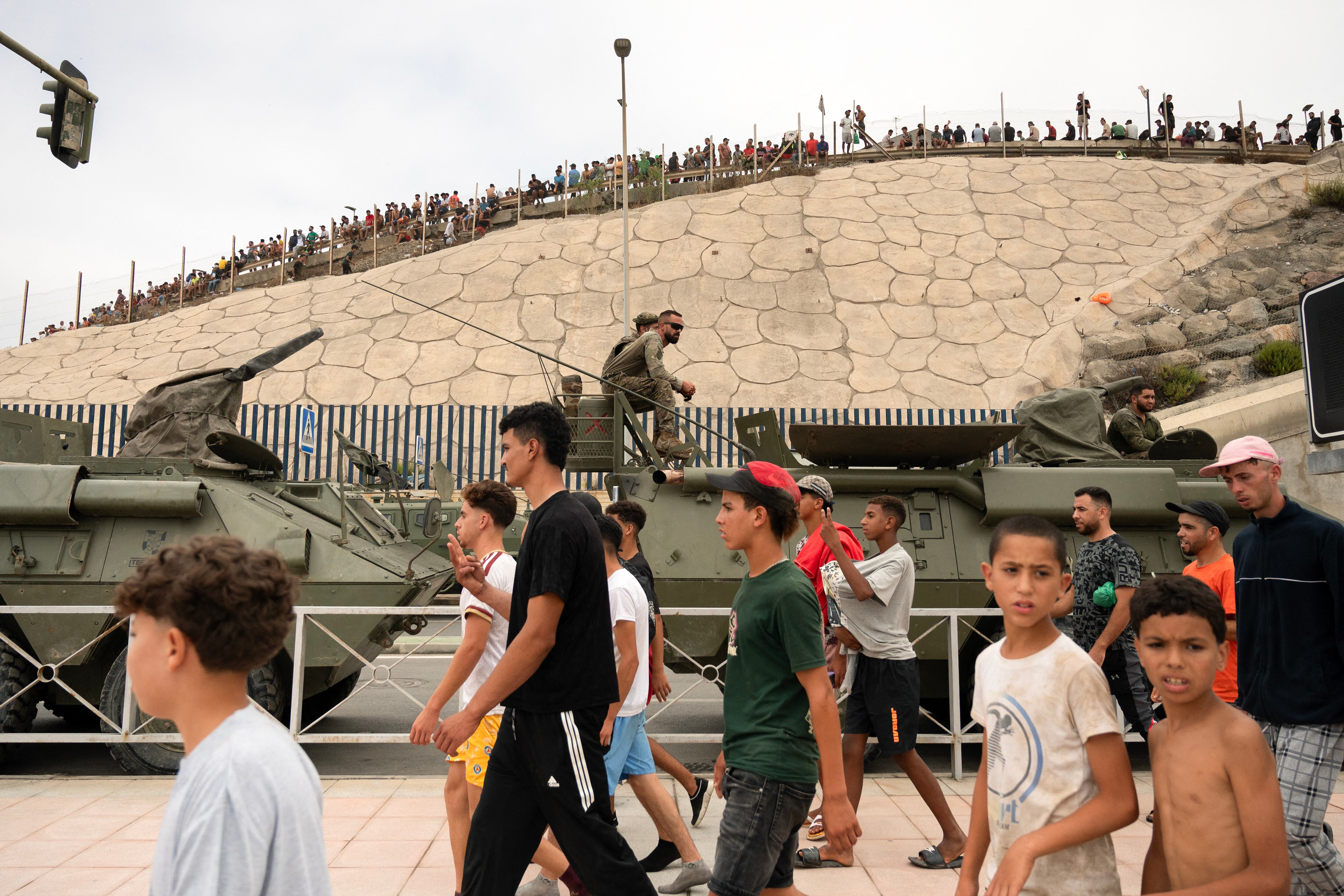 Migrants walk past Spanish military personal in the border between Morocco and the Spain's north Africa's Ceuta enclave on July 31, 2026. Thousands of migrants crossed overnight from Morocco into Ceuta enclave, a police source said, as Spanish Prime Minister was set to arrive to manage the latest migrant crisis on the border. In recent days, a total of around 40,000 migrants have crossed into the territory, population 80,000, the source added. (Photo by Jorge GUERRERO / AFP)