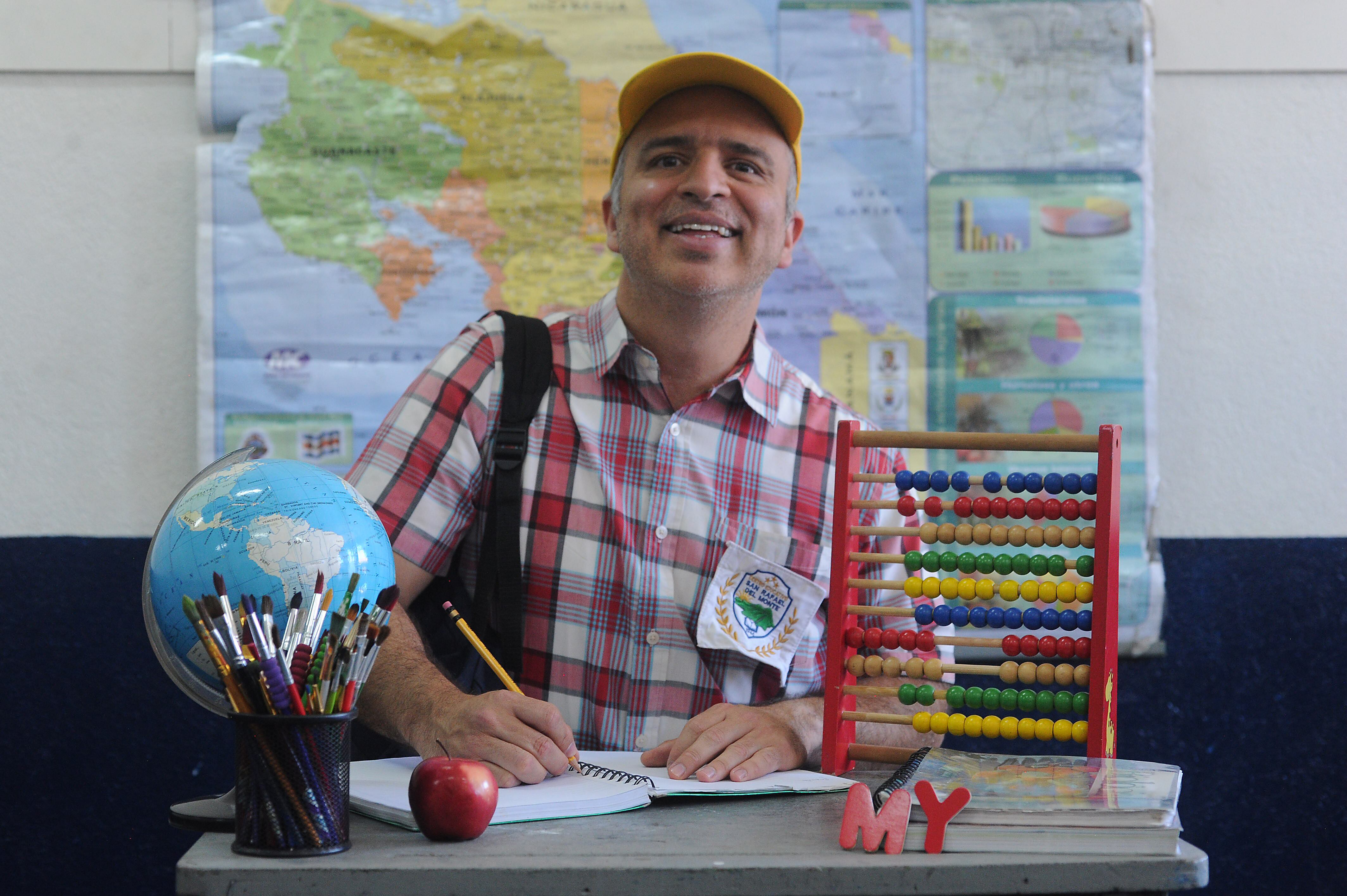 Imagen promocional del personaje Maikol Yordan sentado en un puputre de escuela, con un mapa al fondo, un ábaco y un globo terráqueo.
