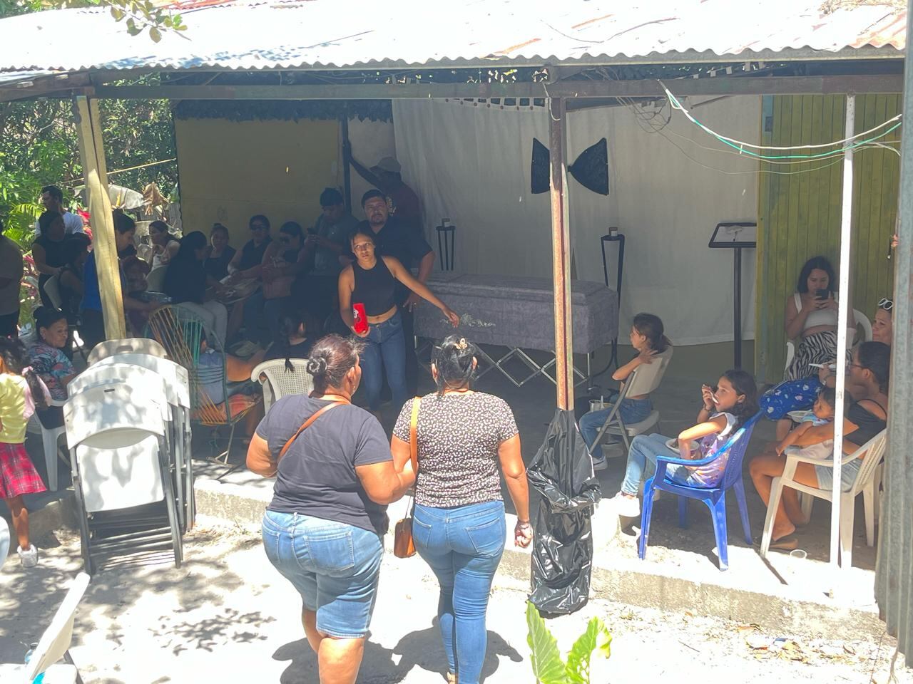 Un funeral en una casa, varias personas llegando, una tumba al fondo.
