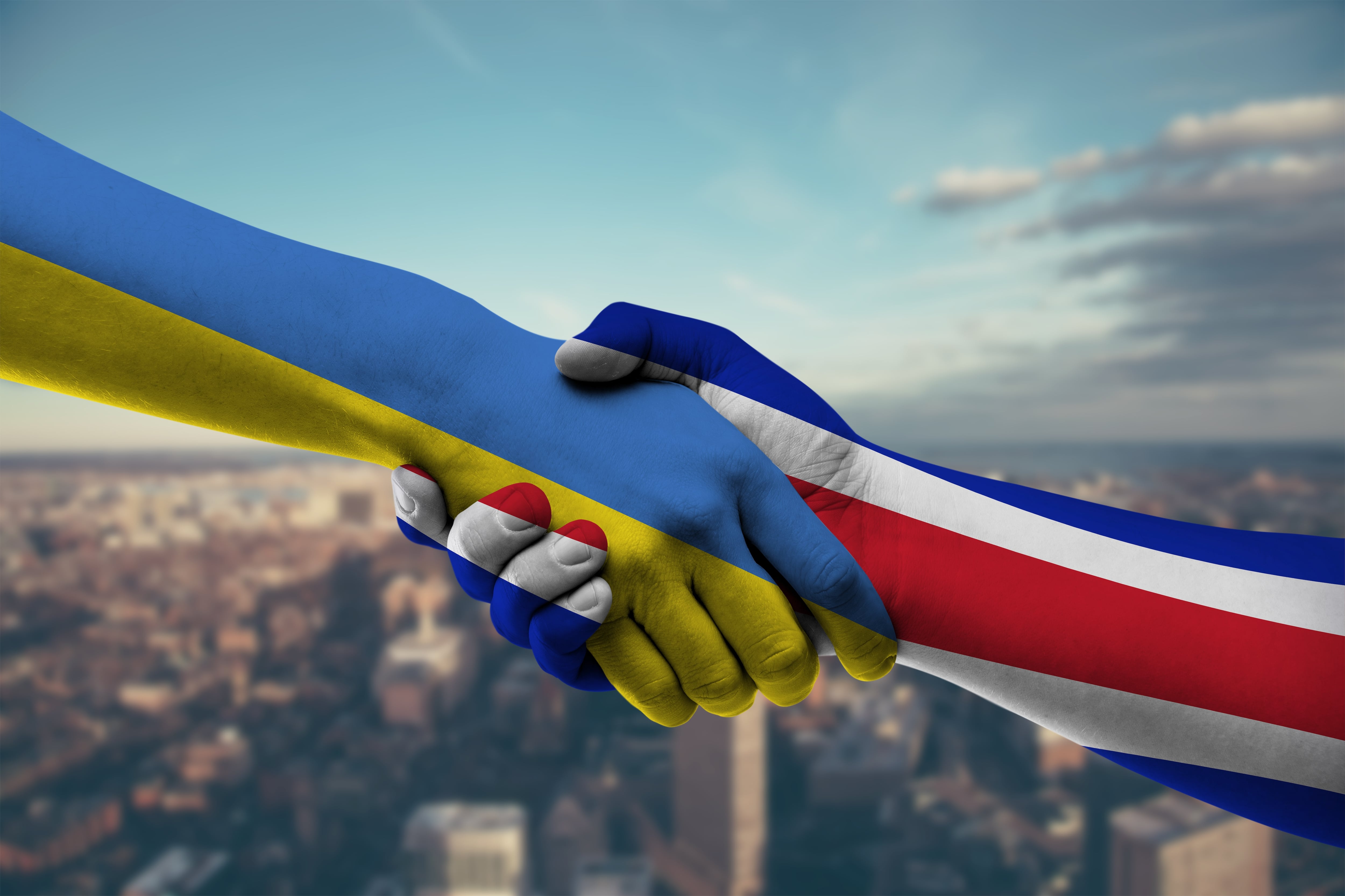 Manos y brazos pintados con las banderas de Ucrania y Costa Rica se estrechan