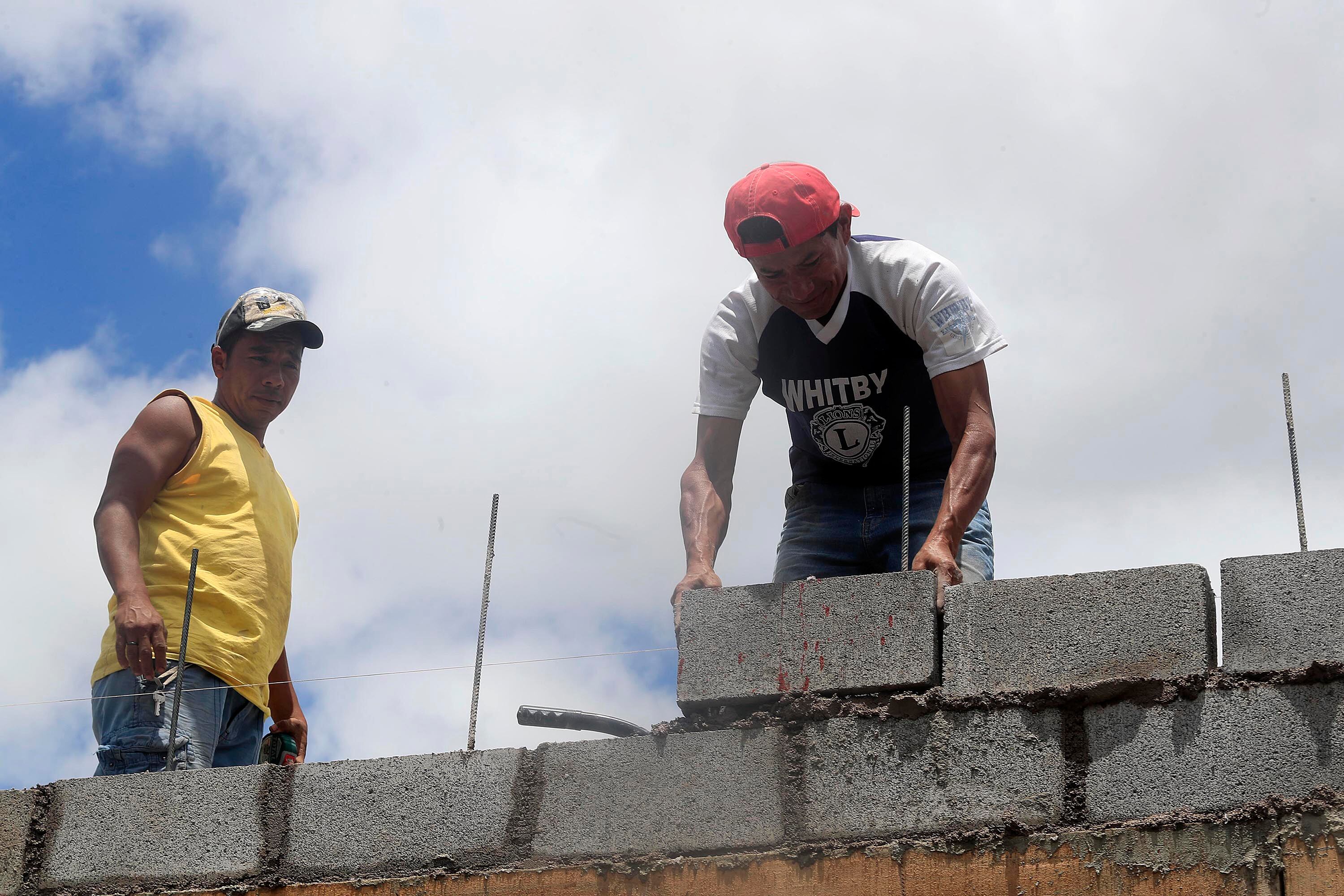 Dos trabajadores de la construcción colocando bloques de concreto en una obra bajo el cielo despejado de Costa Rica.