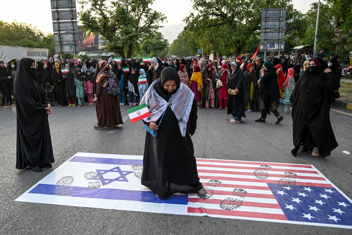 Una mujer musulmana chiita del Majlis Wahdat-e-Muslimeen (MWM) sostiene la bandera de Irán mientras se coloca sobre las banderas de Israel y Estados Unidos durante una protesta contra Israel en Islamabad el 17 de junio de 2025, en medio del conflicto en curso entre Israel e Irán. (Foto: Aamir QURESHI / AFP)