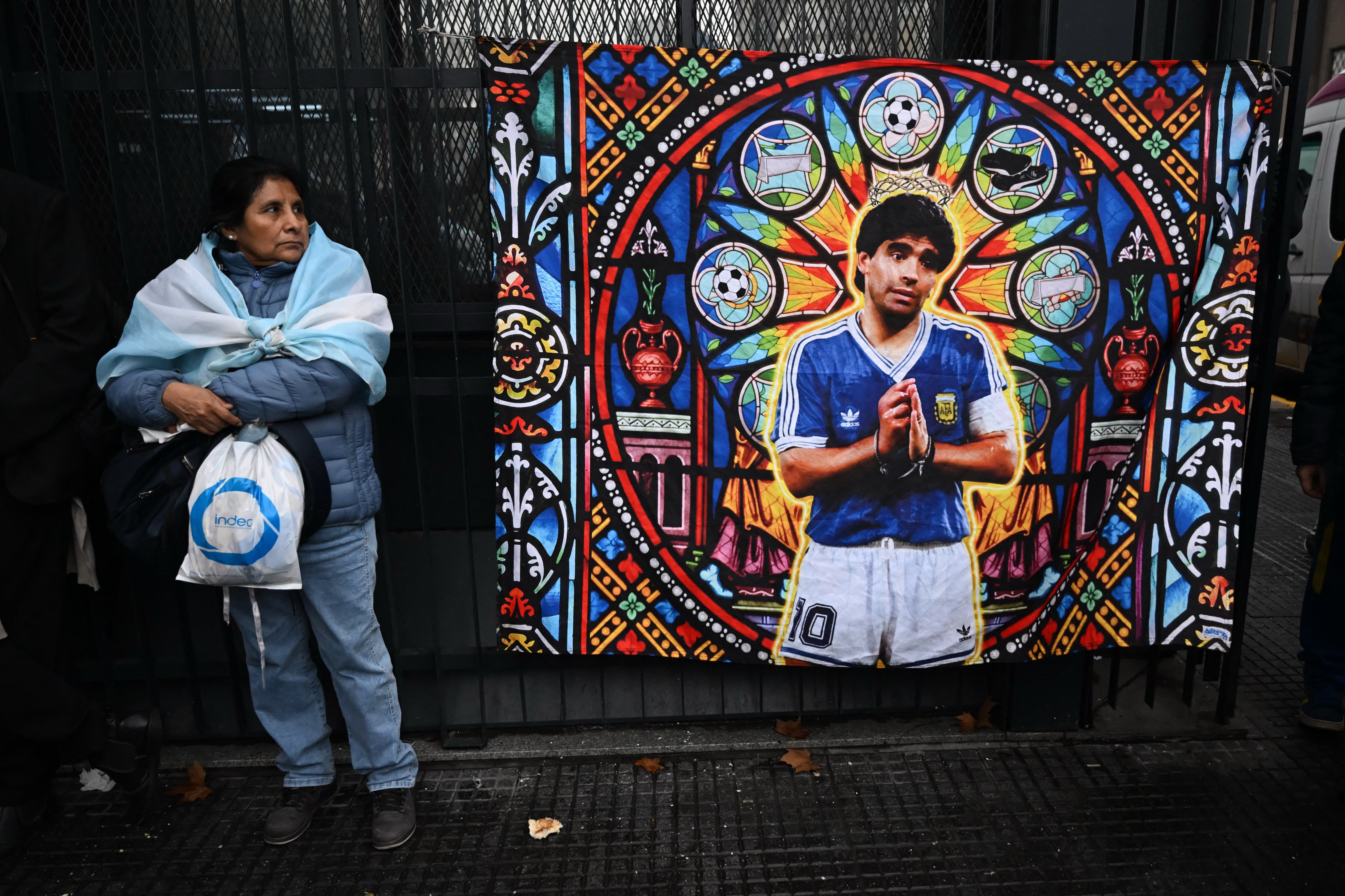 Una mujer permanece junto a esta imagen de Diego Armando Maradona en el centro de Buenos Aires, mientras en la localidad de San Isidro se realiza el juicio por la muerrte del astro.