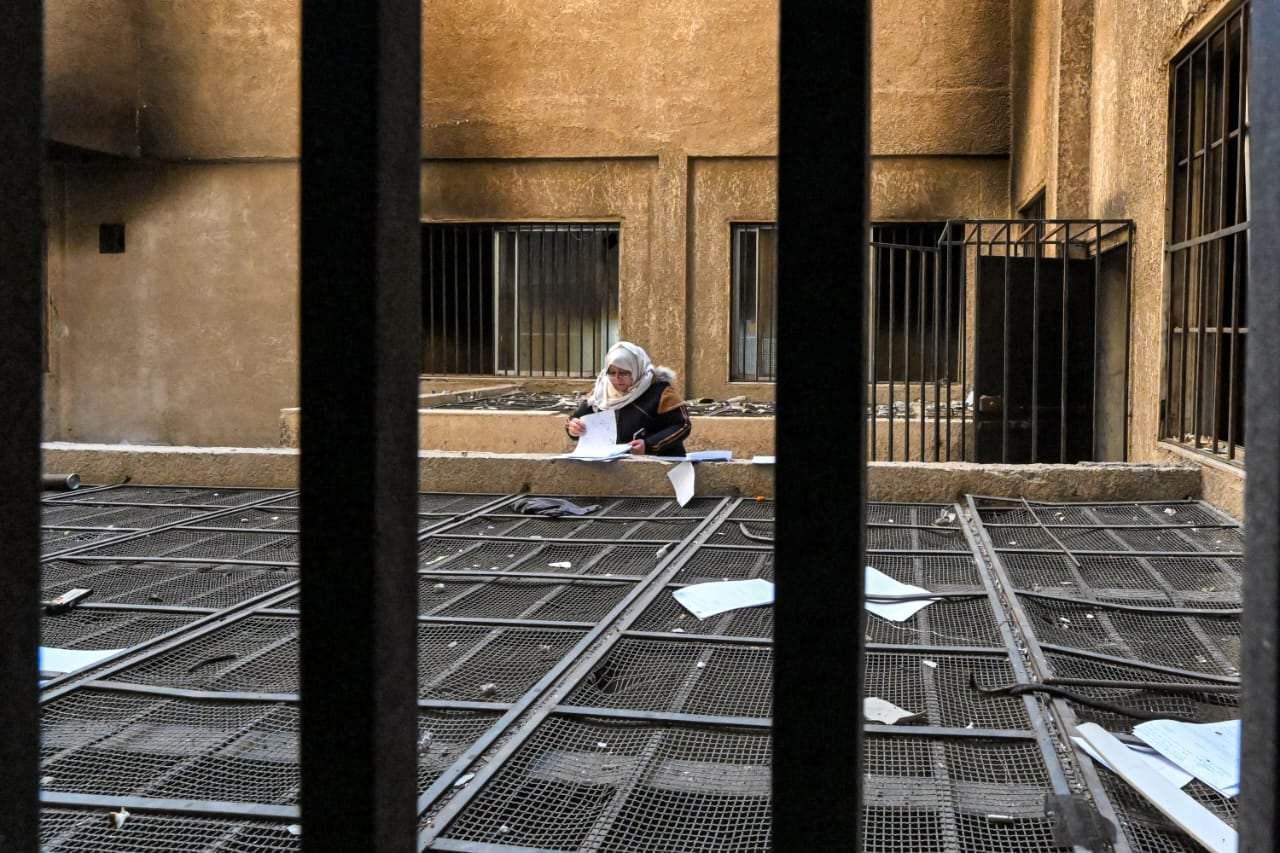 Mujer busca documentos entre rejas de una prisión abandonada en Siria tras la caída de Saidnaya.