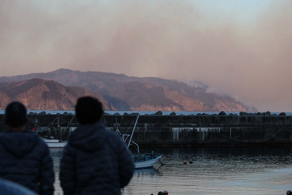 People look out at smoke rising from a forest fire near the city of Ofunato, Iwate Prefecture on February 27, 2025. At least one person has died in a wildfire that damaged more than 80 buildings and forced the evacuation of hundreds of residents in Japan, authorities said on February 27. (Photo by JIJI Press / AFP) / Japan OUT