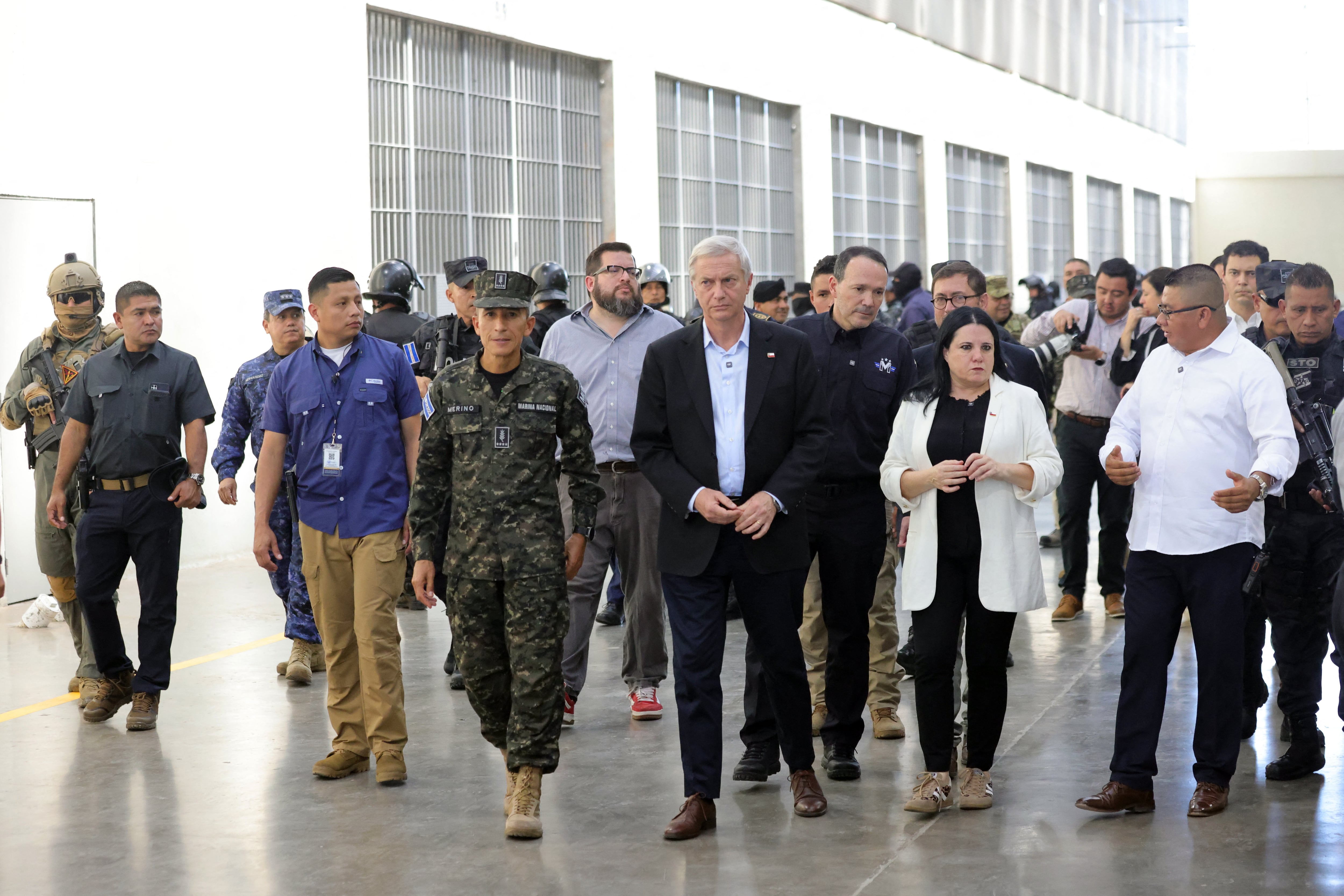El presidente electo de Chile, José Antonio Kast (centro), camina junto al Ministro de Defensa de El Salvador, René Merino Monroy (centro-izquierda), durante una visita a la megacárcel del Centro de Confinamiento del Terrorismo (CECOT),