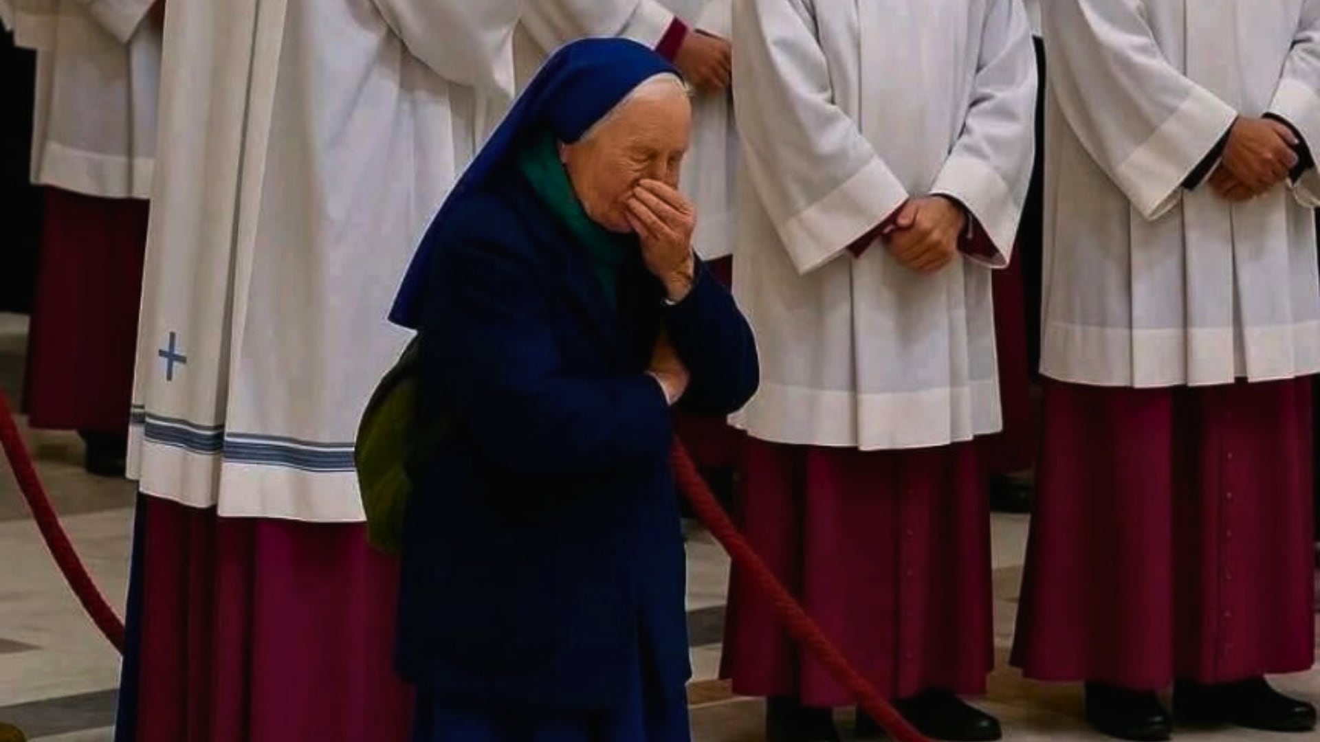 Sor Genevieve Jeanningros, monja de las Hermanitas de Jesús, llora emocionada frente al ataúd del Papa en la basílica de San Pedro, rodeada de clérigos y guardias vaticanos.