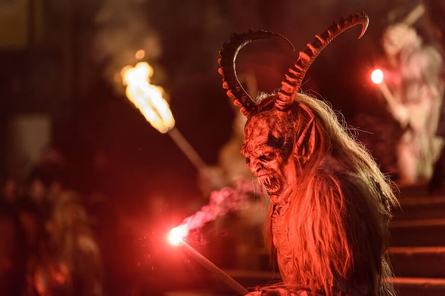 Figura de Krampus con cuernos, sosteniendo una antorcha roja en un desfile nocturno en Austria.