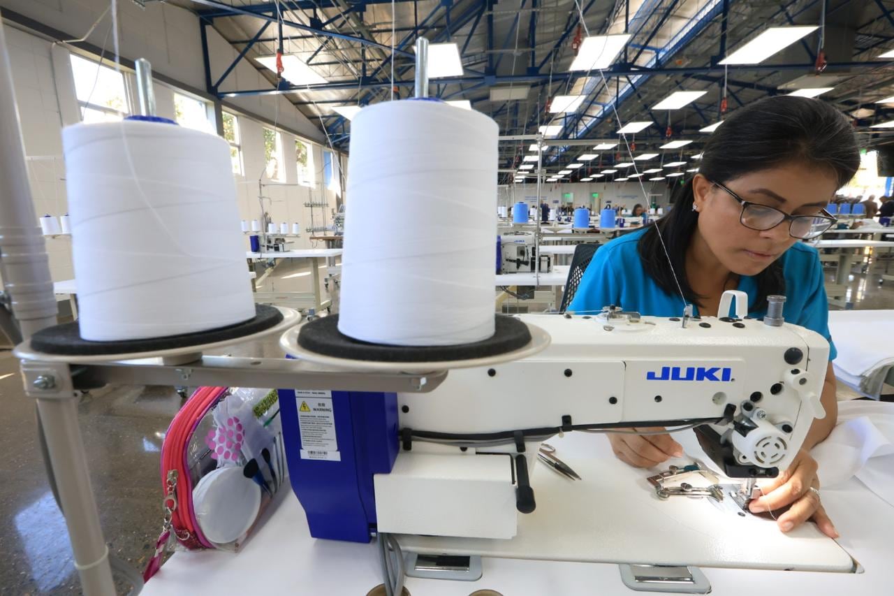 Costurera en su máquina de costura, ella de pelo negro, a los hombros, con anteojos y blusa azul.