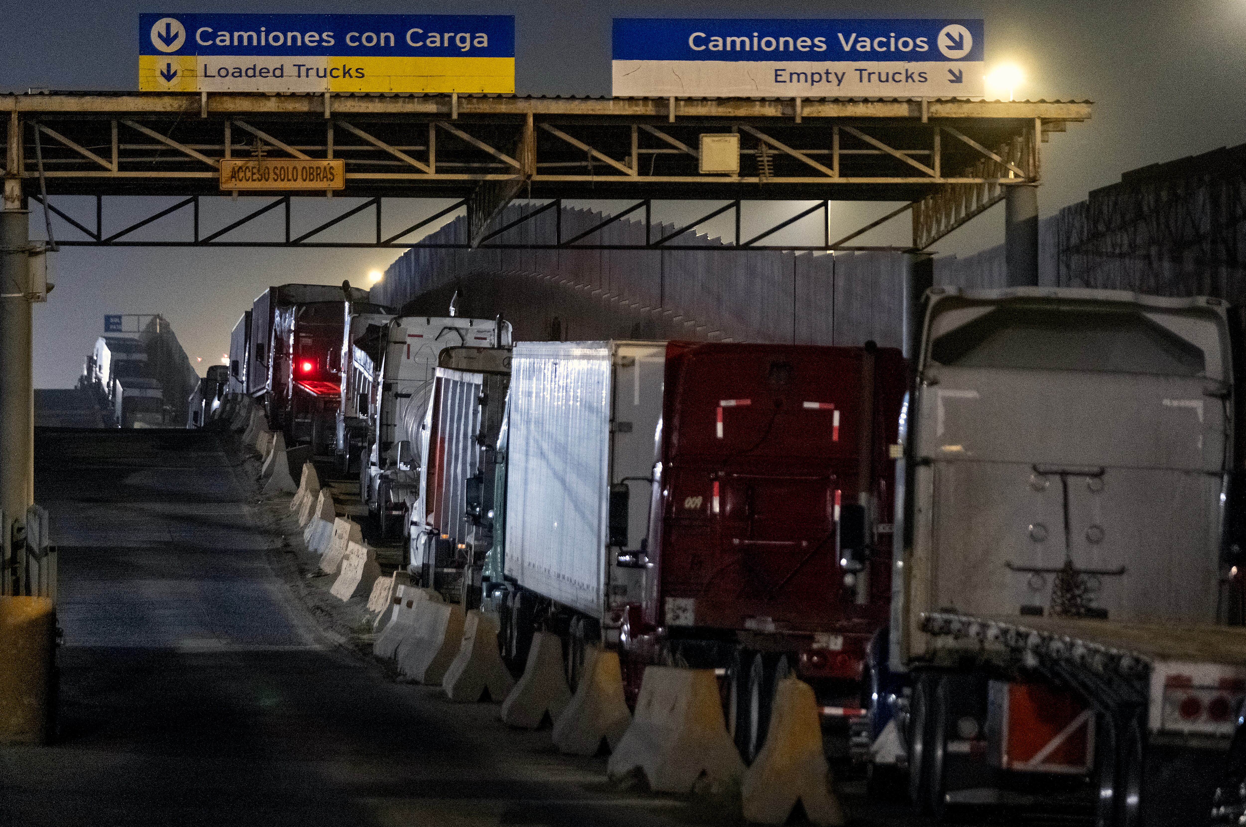 Filas de camiones de carga detenidos en la frontera entre México y Estados Unidos, con señales indicando carriles para camiones vacíos y cargados. La imagen refleja el impacto de los aranceles impuestos por Donald Trump a las exportaciones mexicanas.