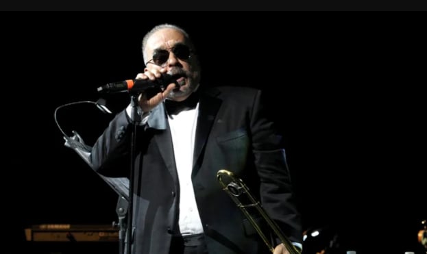 Imagen del salsero Willie Colón usando un traje de color negro y camisa blanca durante un concierto.