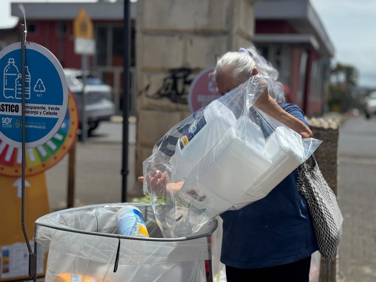 Una mujer deposita material de reciclaje en un basurero.