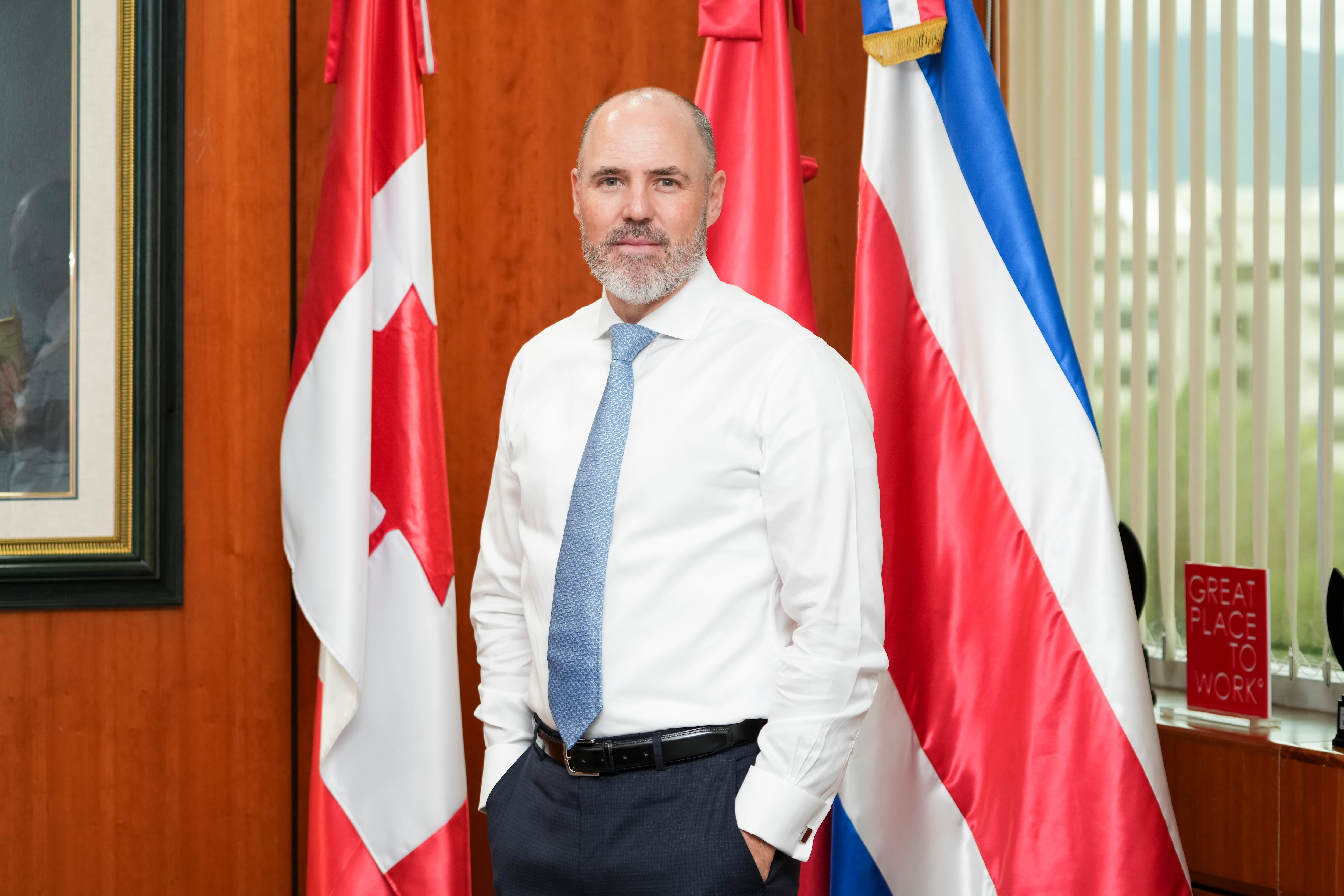 Robert Williams, ejecutivo de Scotiabank, de pie en una oficina junto a las banderas de Canadá y Costa Rica, en el contexto de la integración con Davivienda.