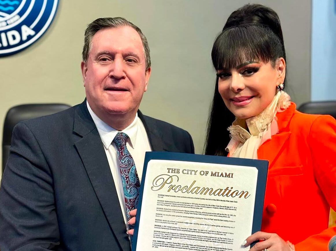 El comisionado de Miami Joe Carollo posa junto a Maribel Guardia en el ayunamiento de Miami, mientras ella sostiene la proclama que declara el 30 de diciembre como día en su honor