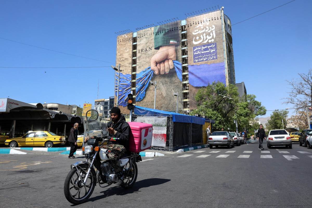 A man rides past a large billboard referring to the Strait of Hormuz in Tehran's Vanak Square on April 15, 2026.
