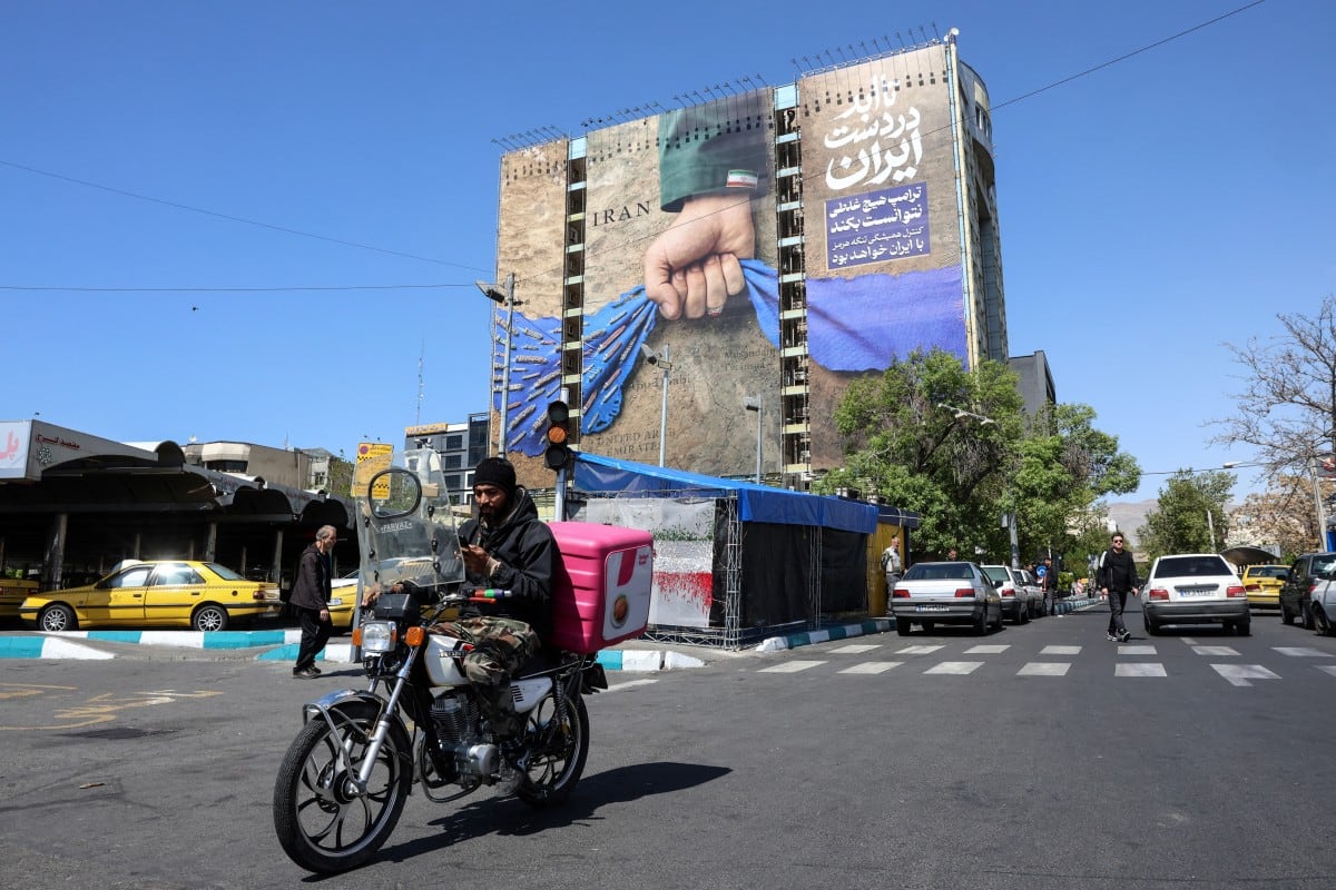 A man rides past a large billboard referring to the Strait of Hormuz in Tehran's Vanak Square on April 15, 2026.