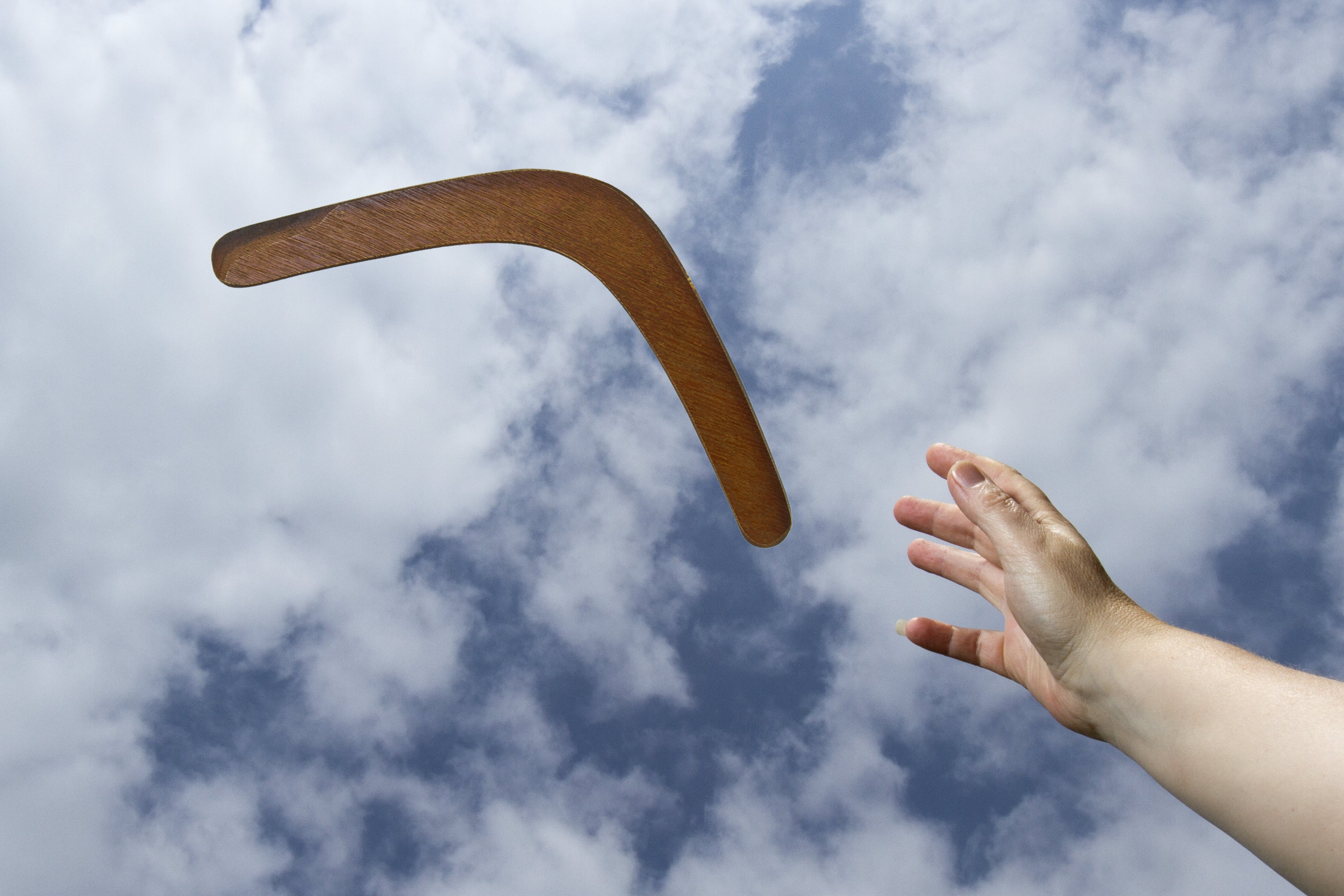 Efecto bumerán. Mano lanzando bumerán contra cielo con nubes. Boomerang