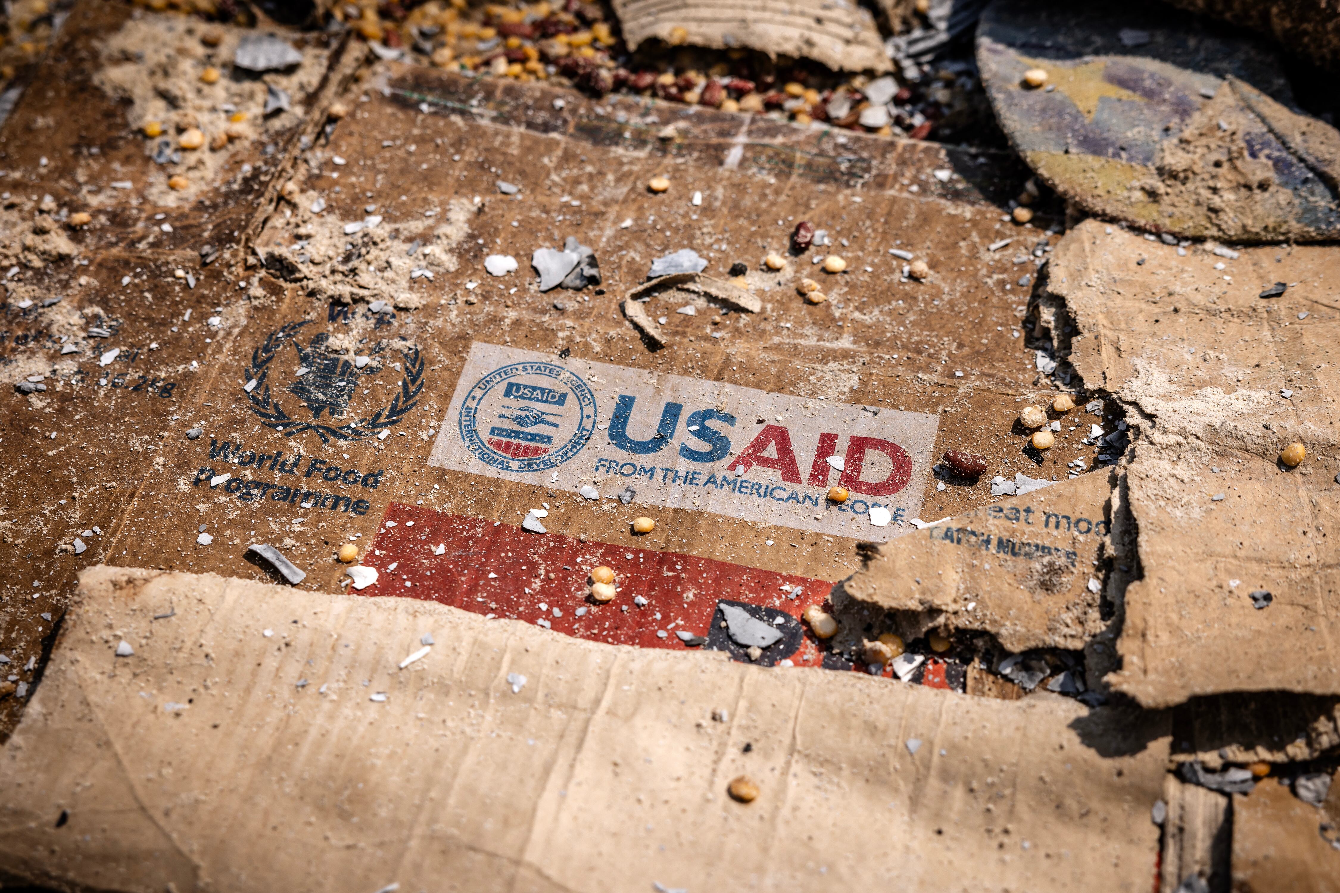 Un logotipo de USAID es visible en una caja entre restos dispersos.