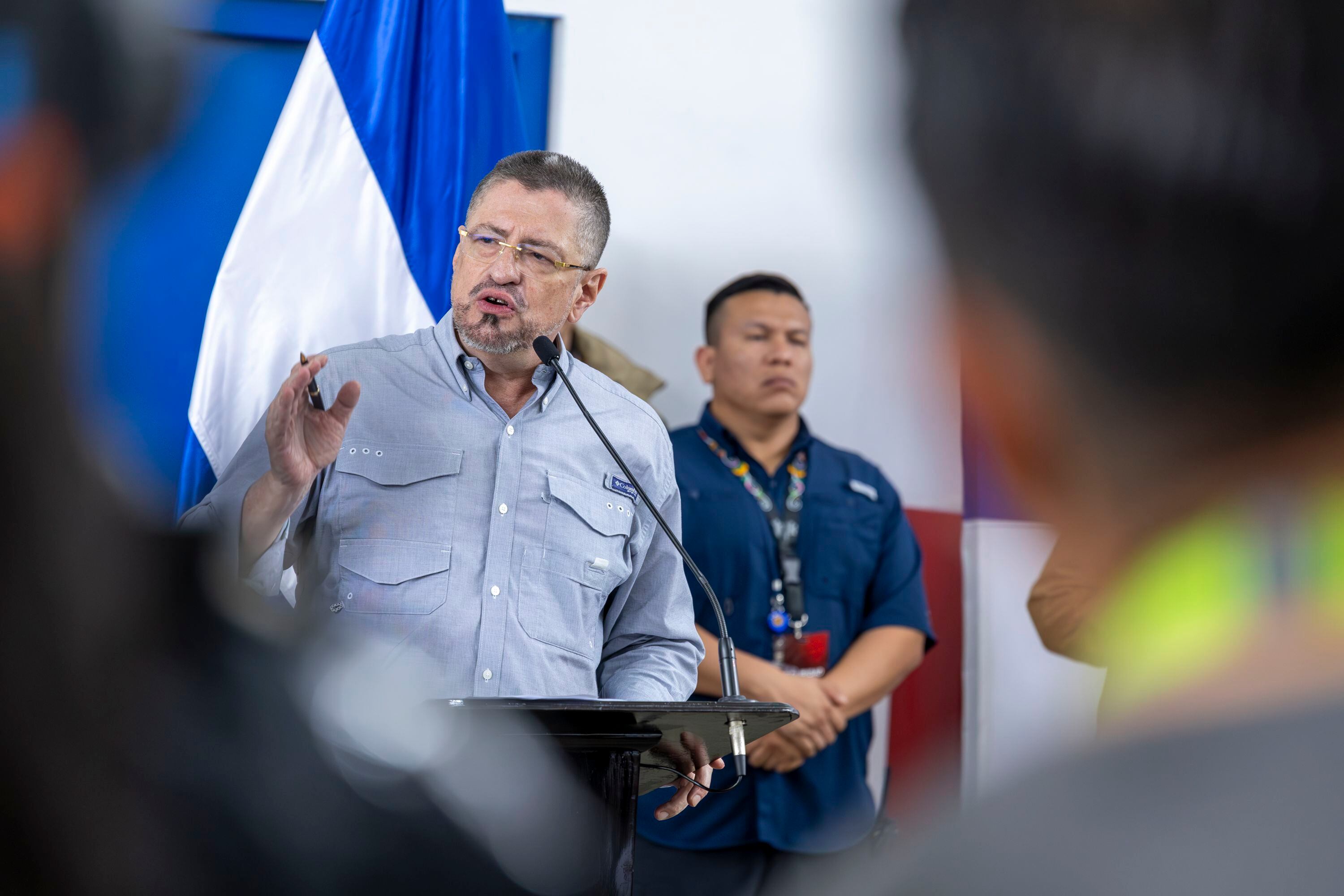 El presidente de Costa Rica, Rodrigo Chaves, se dirige a la prensa, acompañado por un colaborador, con la bandera de El Salvador al fondo, durante la visita del mandatario salvadoreño Nayib Bukele.