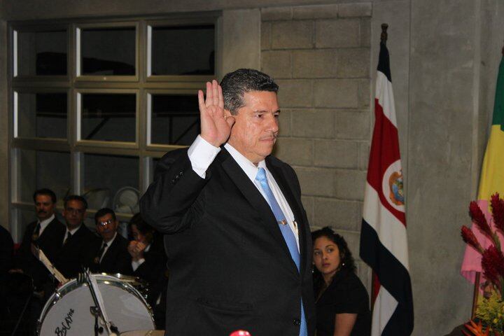 El exalcalde de Santa Ana, Gerardo Oviedo, juramentando en un acto oficial, con la bandera de Costa Rica al fondo y asistentes en la ceremonia.