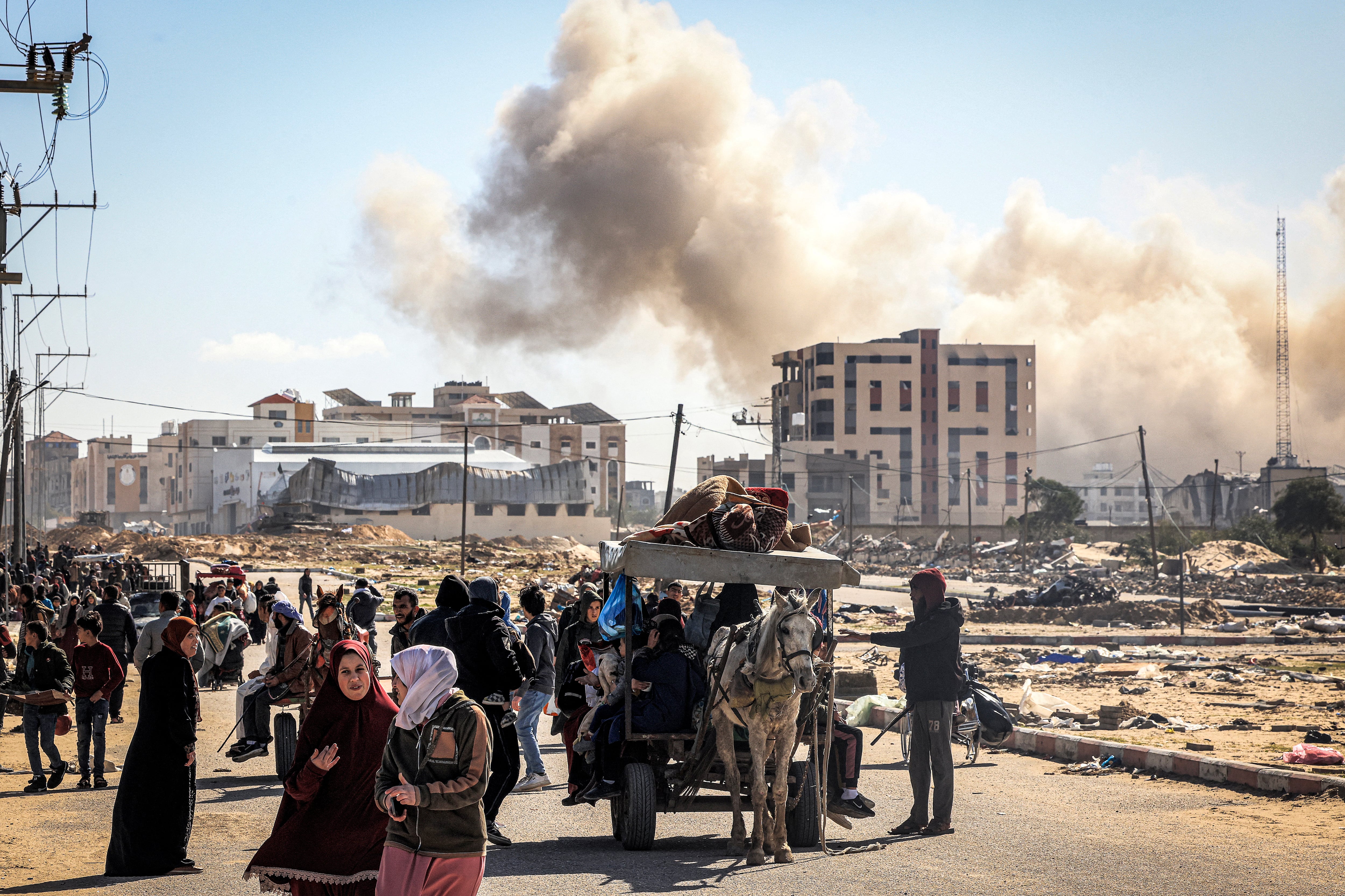 El humo de los bombardeos se eleva al fondo mientras los palestinos desplazados huyen de Khan Yunis, en el sur de la Franja de Gaza.