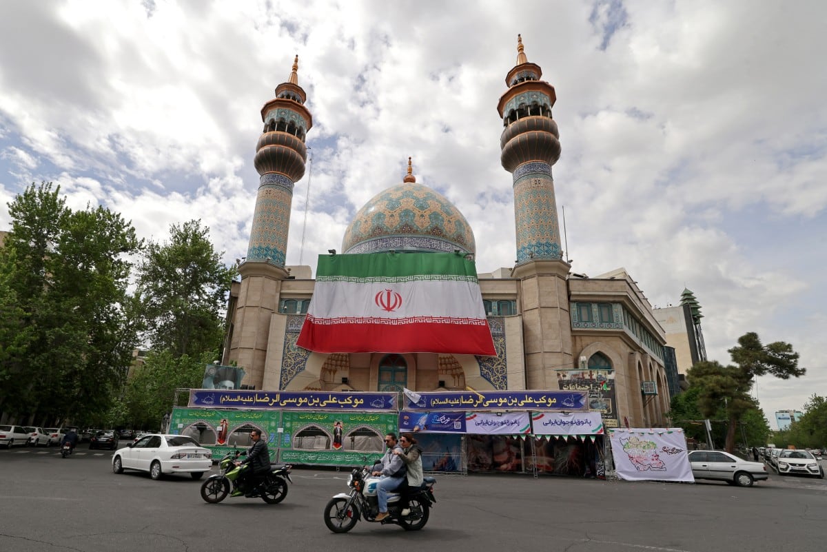 Automovilistas pasan frente a la mezquita Imam Sadiq (AS), con una enorme bandera iraní instalada en su fachada, en la plaza Palestina de Teherán el 19 de abril de 2026.