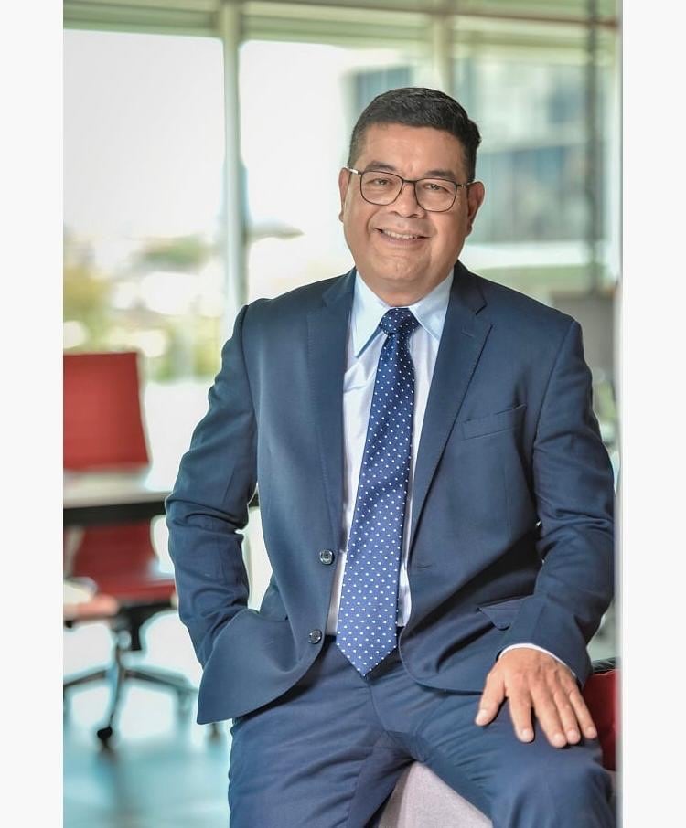 El periodista pensionado Marcelo Castro usando un traje y corbata azul y camisa blanca. Sonríe hacia la cámara.