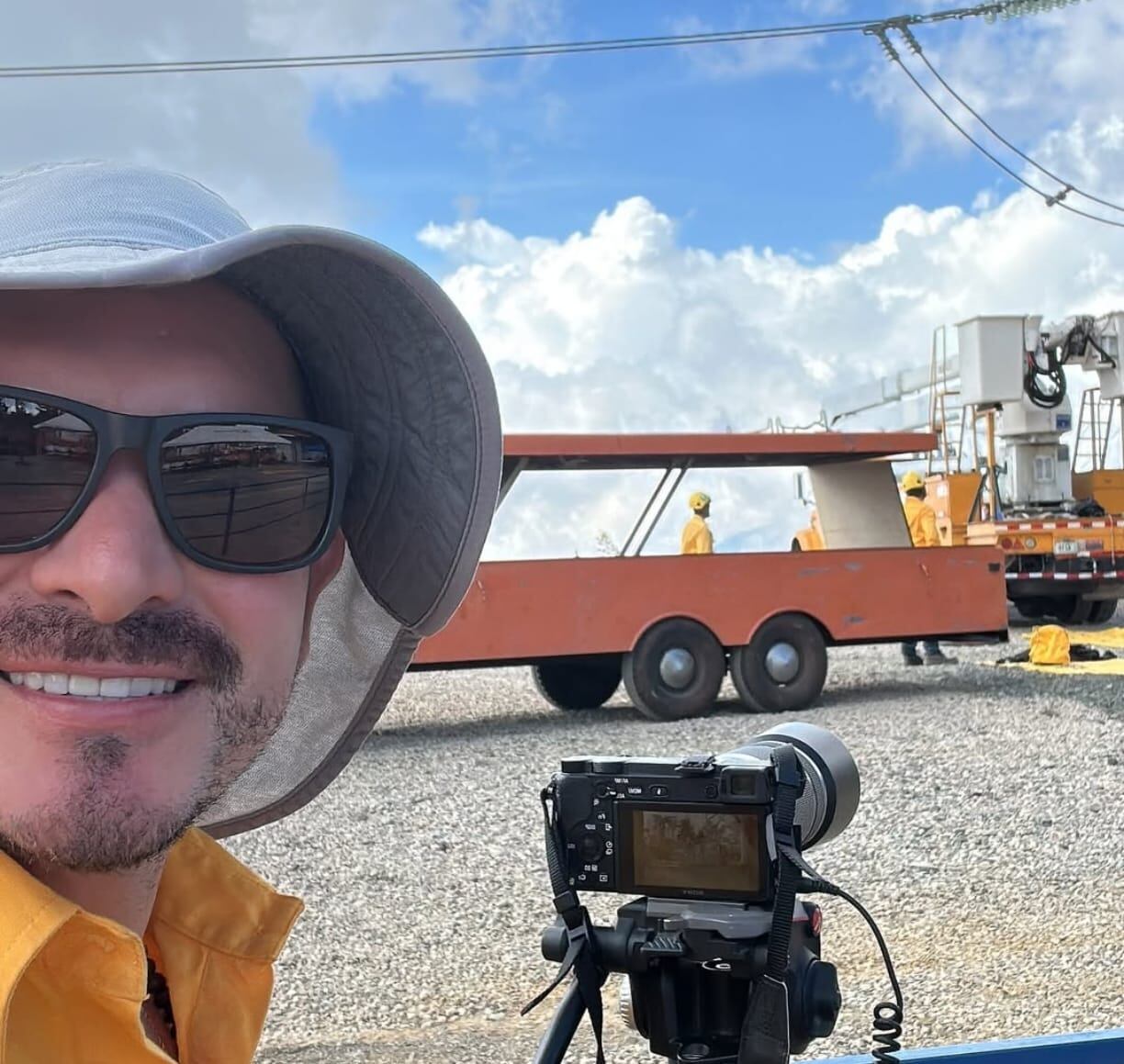 El periodista José Ernesto Herrera con una cámara, usa sombrero y lentes oscuros.