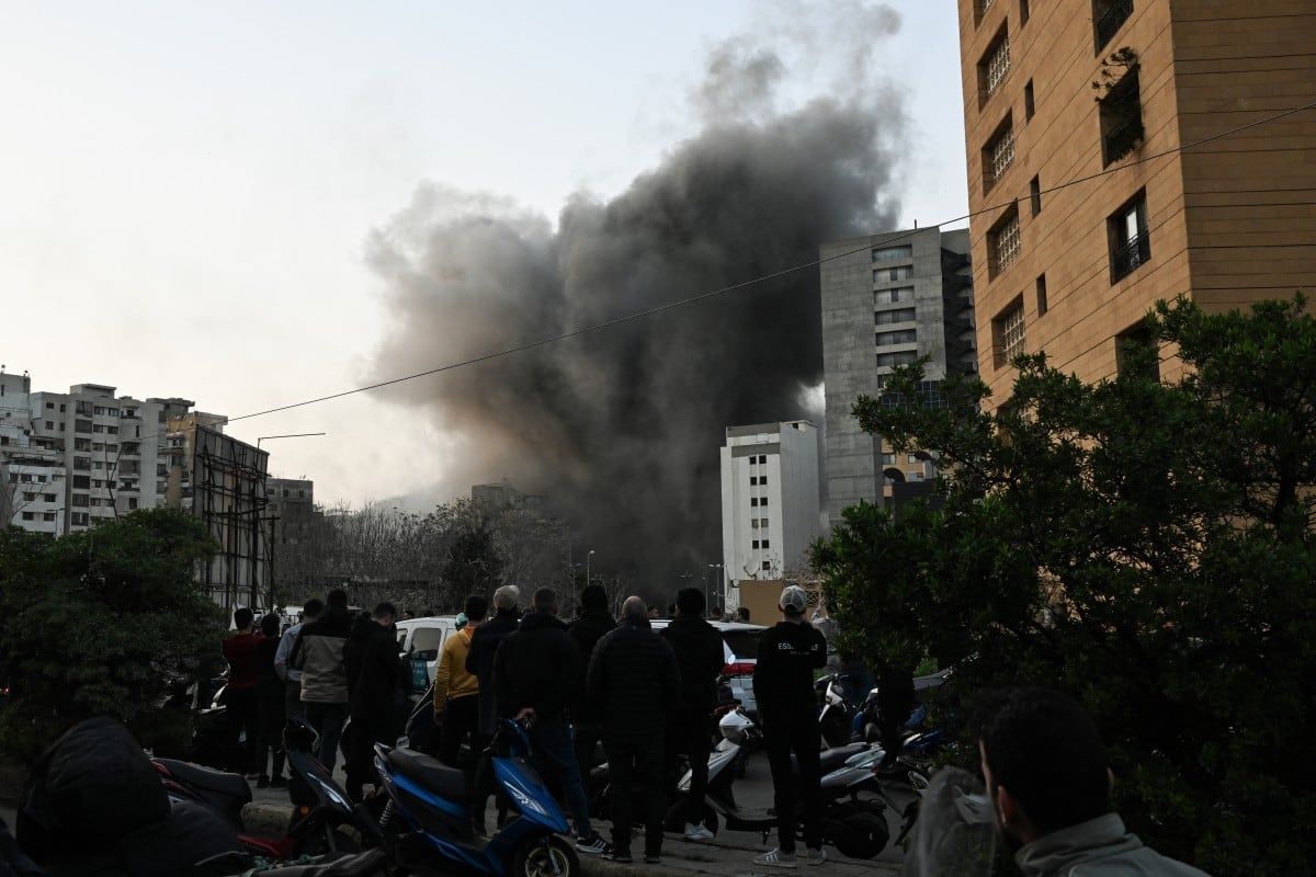 Personas observan una columna de humo que se eleva tras un ataque con misiles israelíes en el barrio de Bashoura, en el centro de Beirut, el 12 de marzo de 2026.