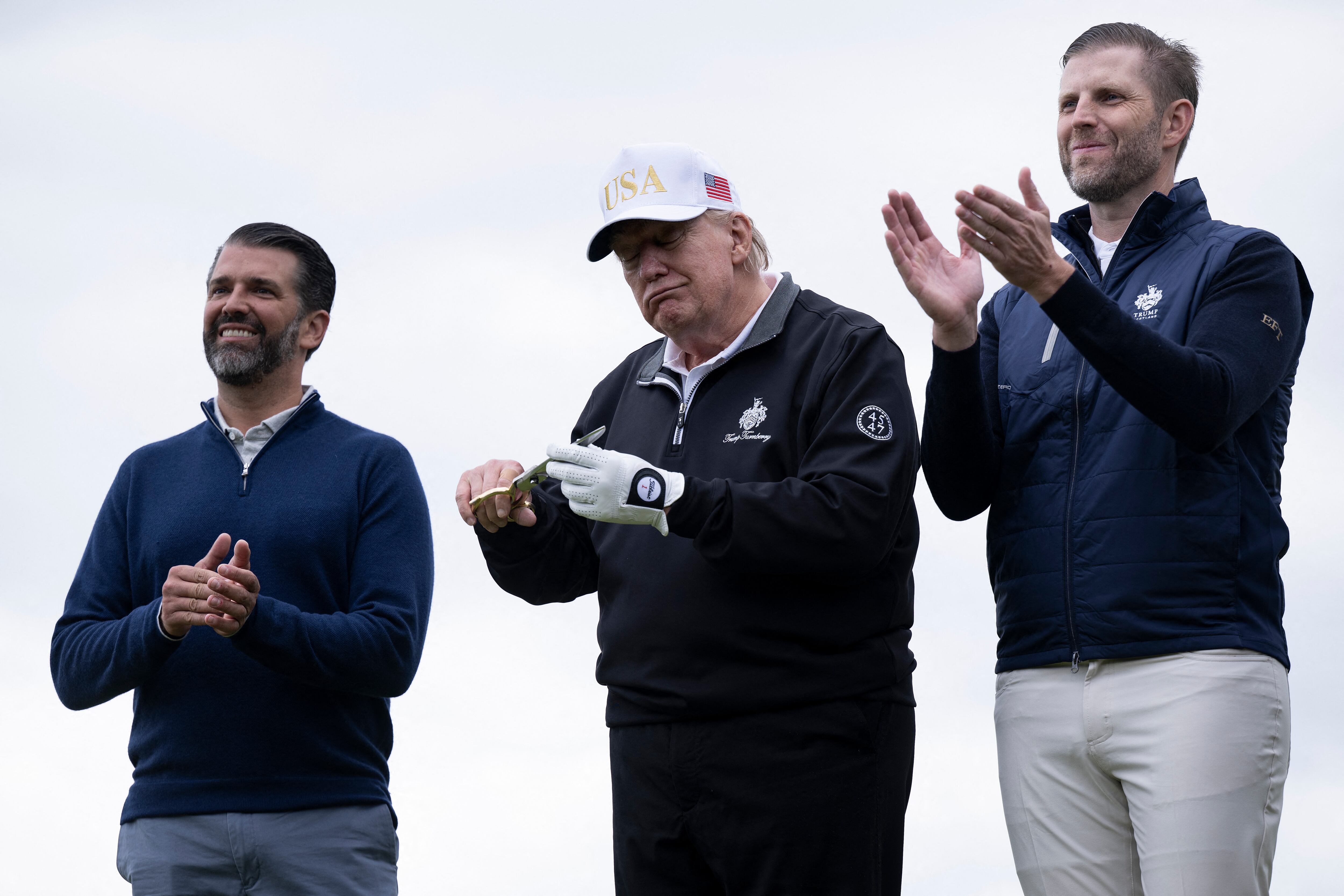 US President Donald Trump (C), flanked by his sons Eric Trump (R) and Donald Trump Jr. (L) cuts the ribbon on the first tee to officially open the Trump International Golf Links course in Balmedie, Aberdeenshire, north east Scotland on July 29, 2025. (Photo by Brendan Smialowski / AFP)