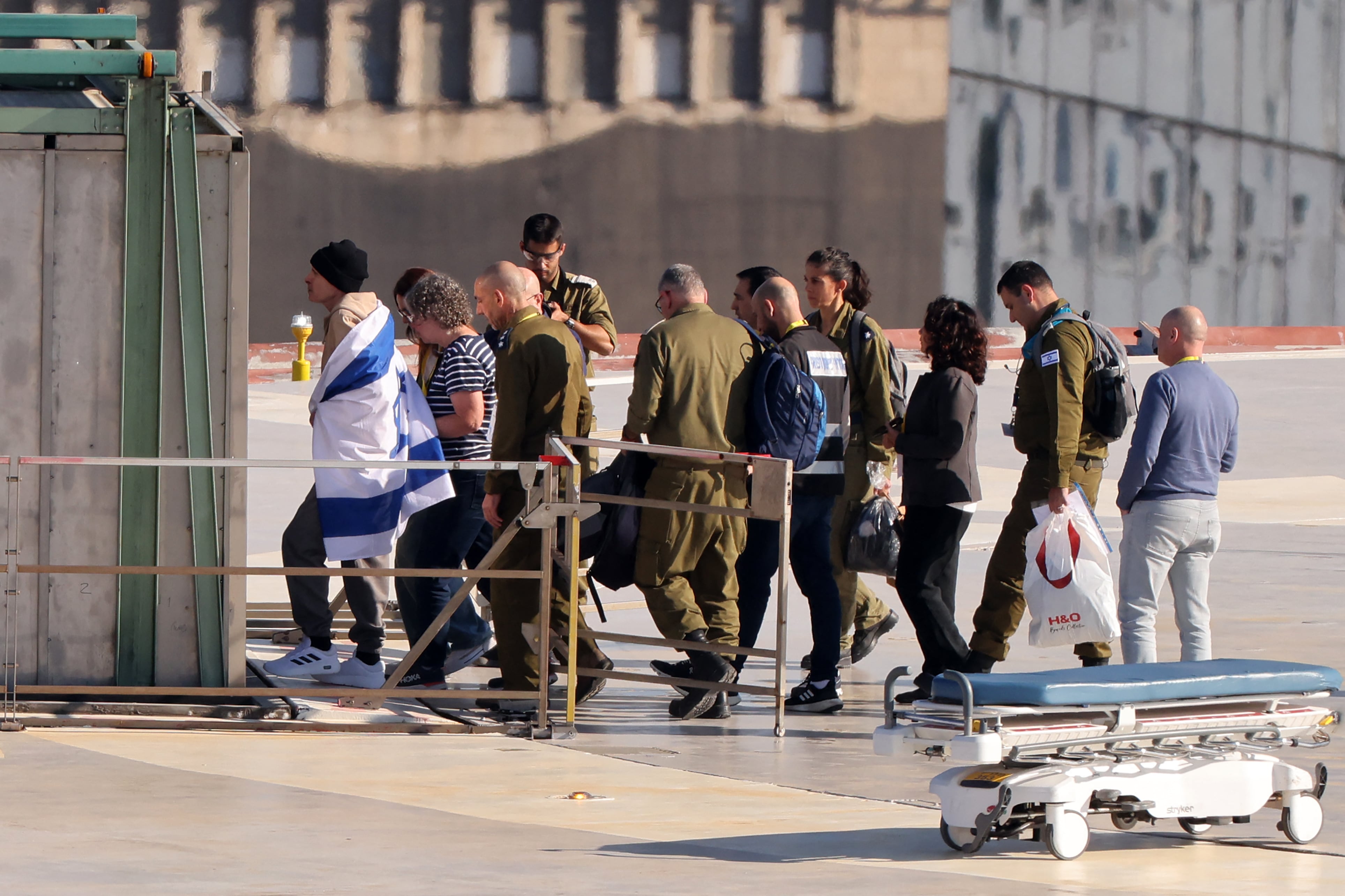 Keith Siegel (izq.), rehén israelí recién liberado y envuelto en una bandera, acompañado de su esposa Aviva (camiseta a rayas), camina al desembarcar de un helicóptero militar en el Centro Médico Sourasky de Tel Aviv.