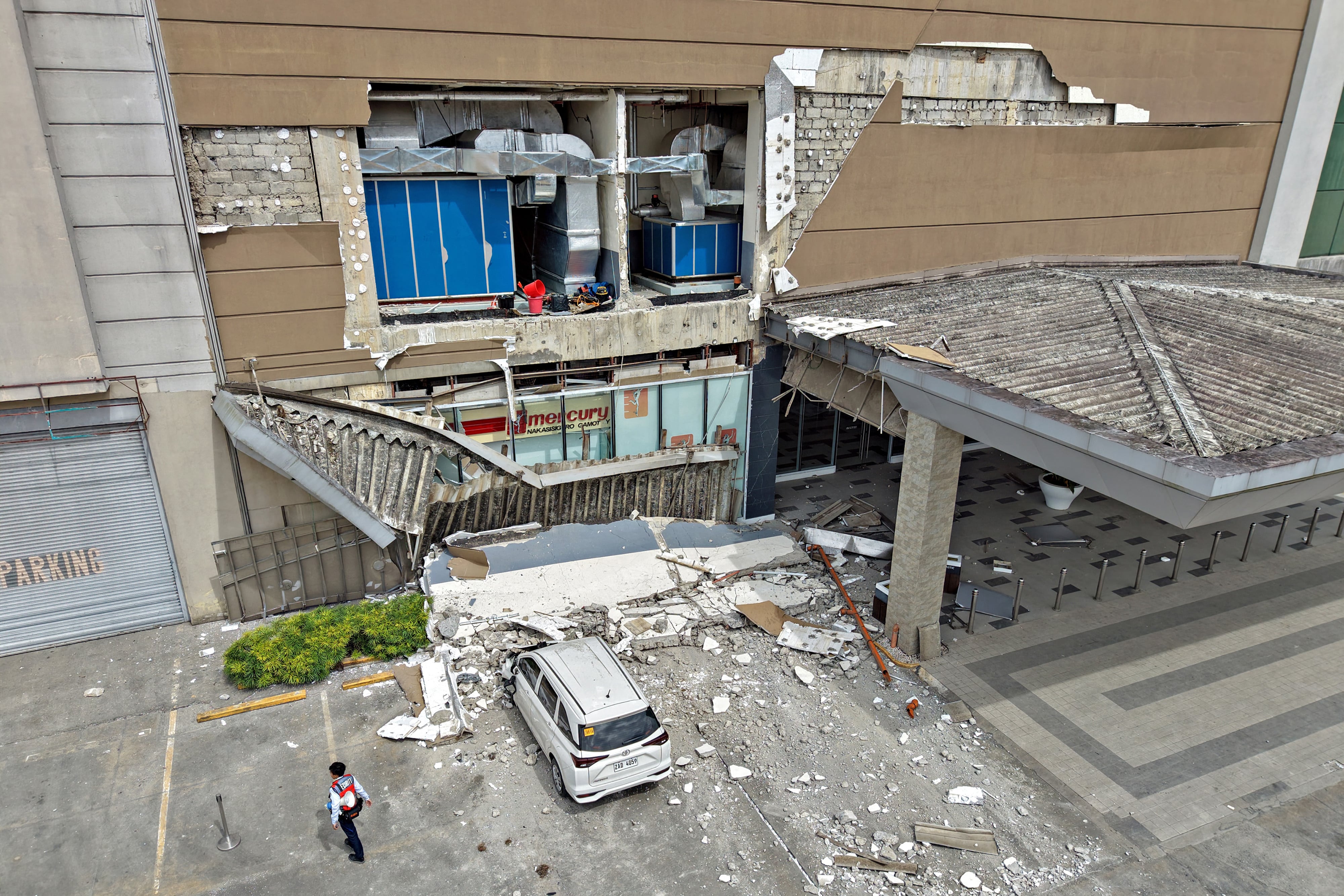 Un guardia de seguridad pasa junto a un muro dañado y un coche frente a un centro comercial en la ciudad de Butuan, en la isla meridional de Mindanao, este viernes 10 de octubre, tras un terremoto de magnitud 7,4 que azotó el sur de Filipinas. Fotografía: