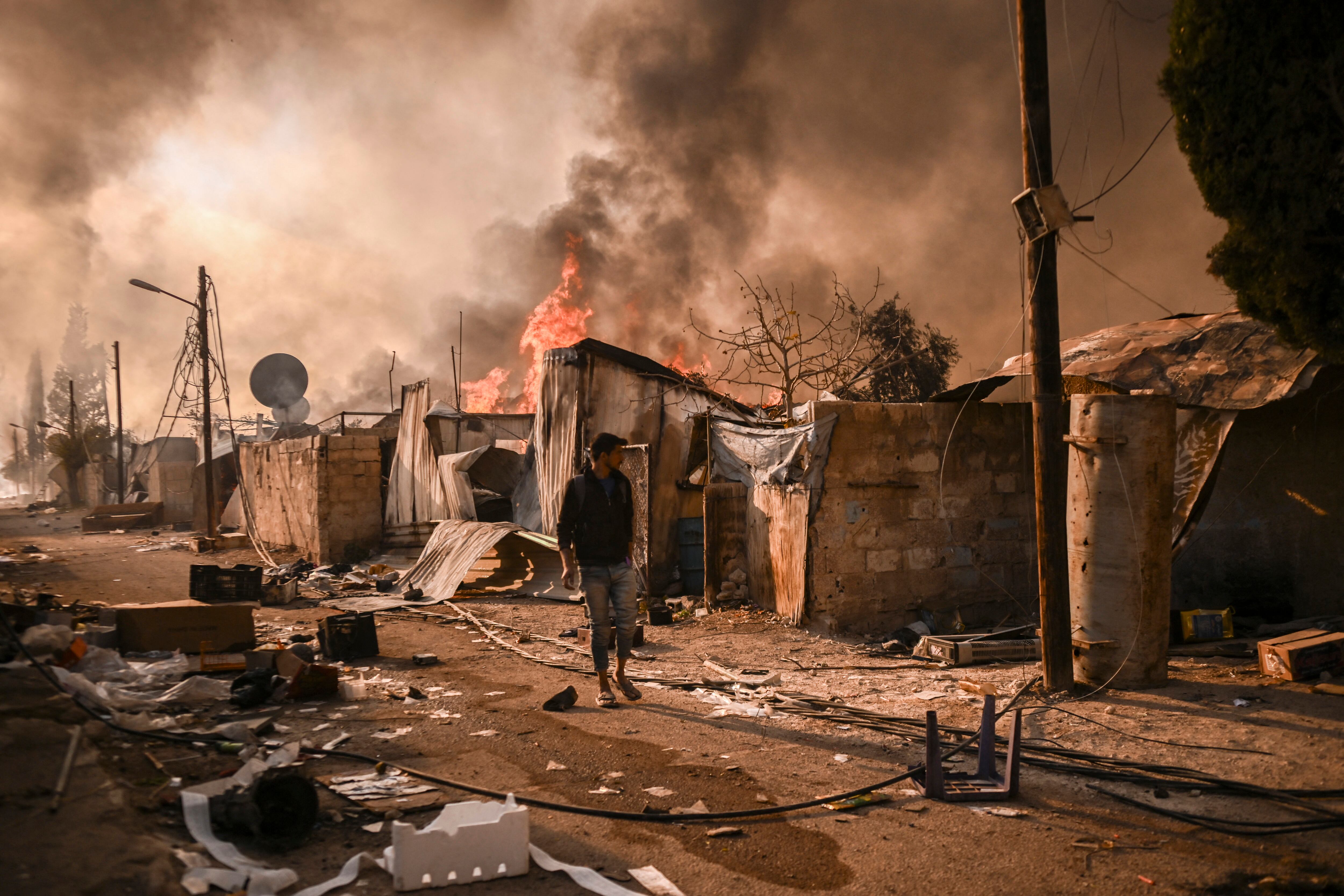 Vista de un complejo de viviendas militares incendiado en Najha, al sureste de Damasco, con una persona caminando entre los escombros y humo denso tras la toma de la ciudad por rebeldes islamistas en Siria.
