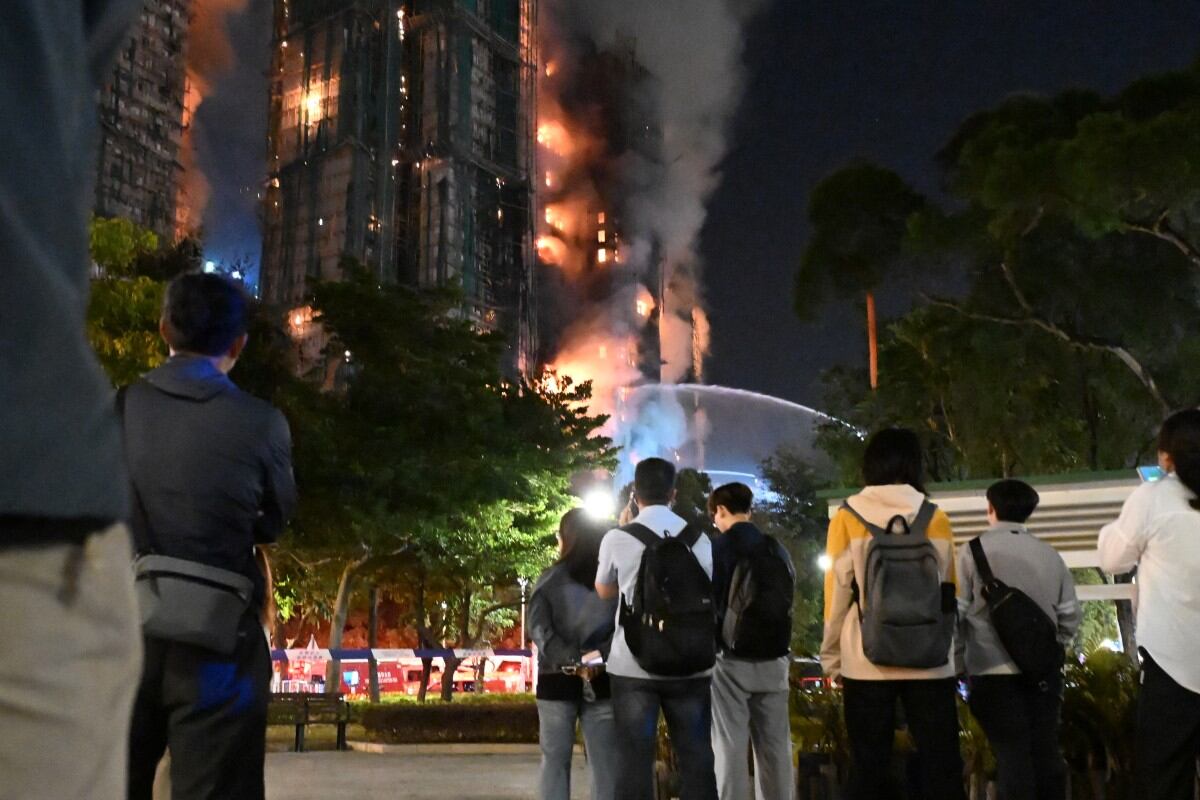 Bystanders look on as thick smoke and flames rise during a major fire at the Wang Fuk Court residential estate in Hong Kong's Tai Po district on November 26, 2025. At least 13 people have died as a result of a raging fire that tore through several high-rise blocks in a Hong Kong residential estate on November 26, a government official said. (Photo by Peter PARKS / AFP)