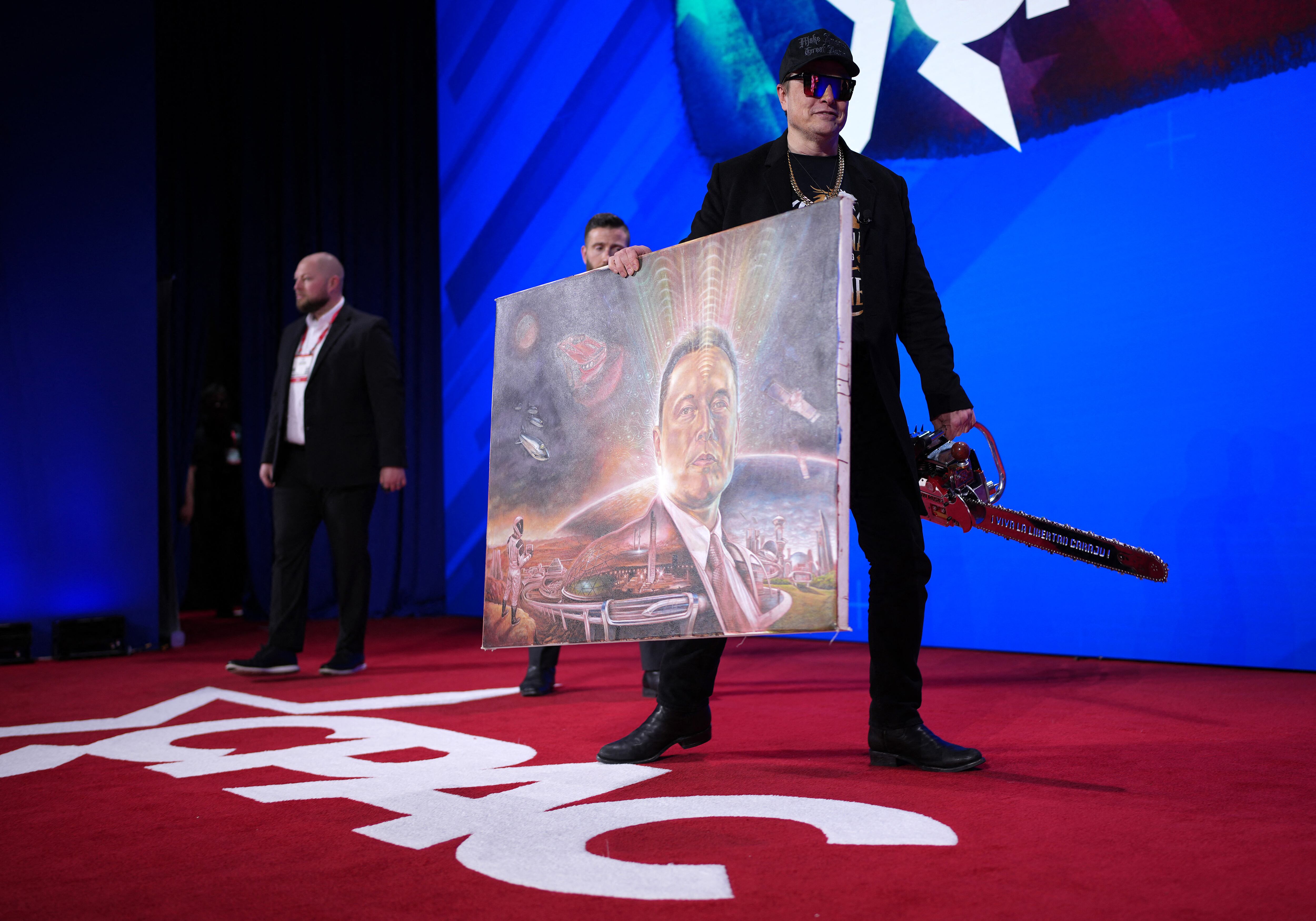 Elon Musk, director ejecutivo de Tesla y SpaceX, sostiene una motosierra y una pintura de sí mismo que le regaló un miembro de la audiencia mientras abandona el escenario después de hablar en la Conferencia de Acción Política Conservadora (CPAC, por sus siglas en inglés)