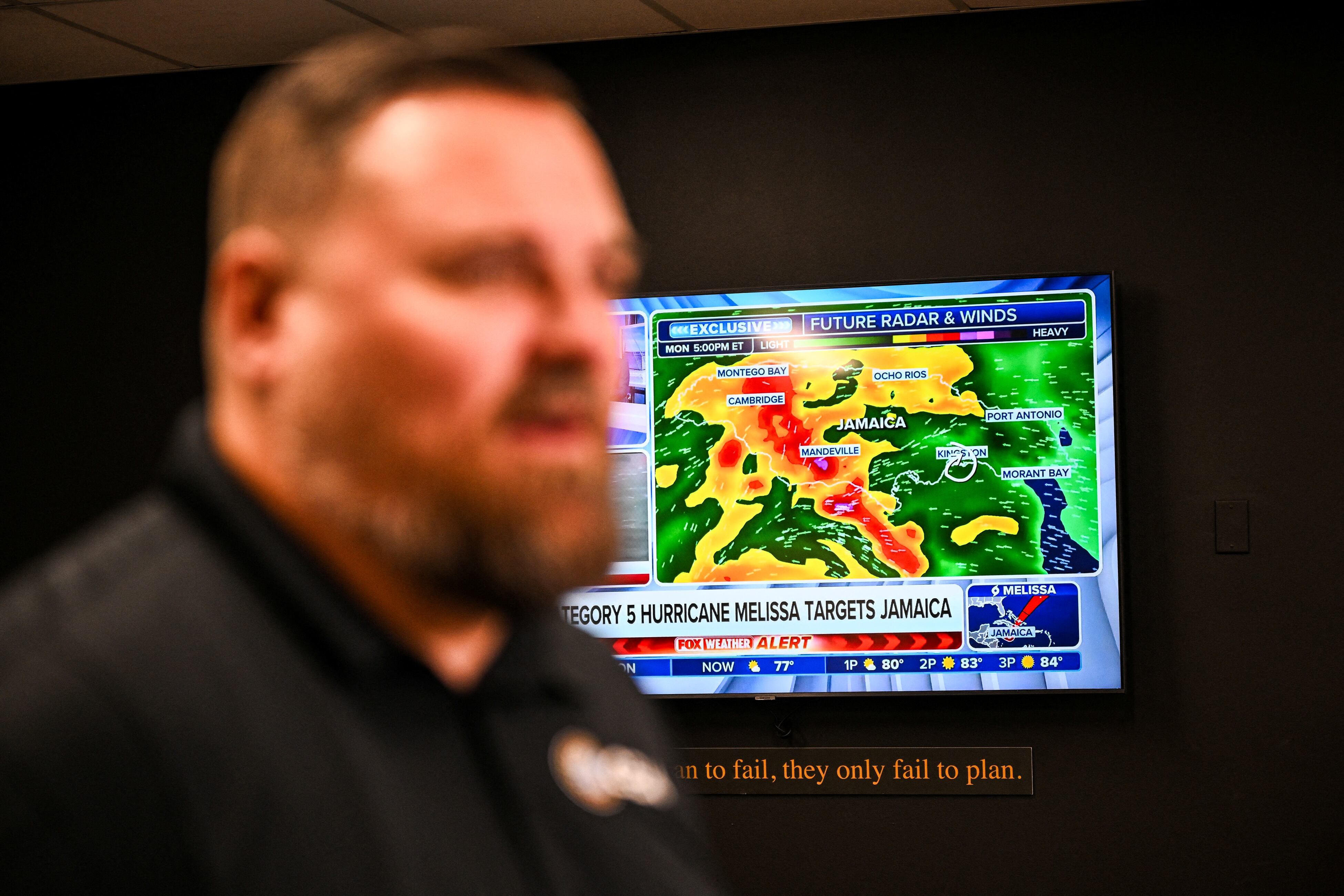 Un canal de noticias meteorológicas muestra actualizaciones sobre el huracán Melissa mientras Billy Richardson, director de almacenamiento en Estados Unidos de Global Empowerment Mission, habla durante una entrevista con AFP en la sede de Global Empowerment Mission en Miami, Florida, el 27 de octubre de 2024.