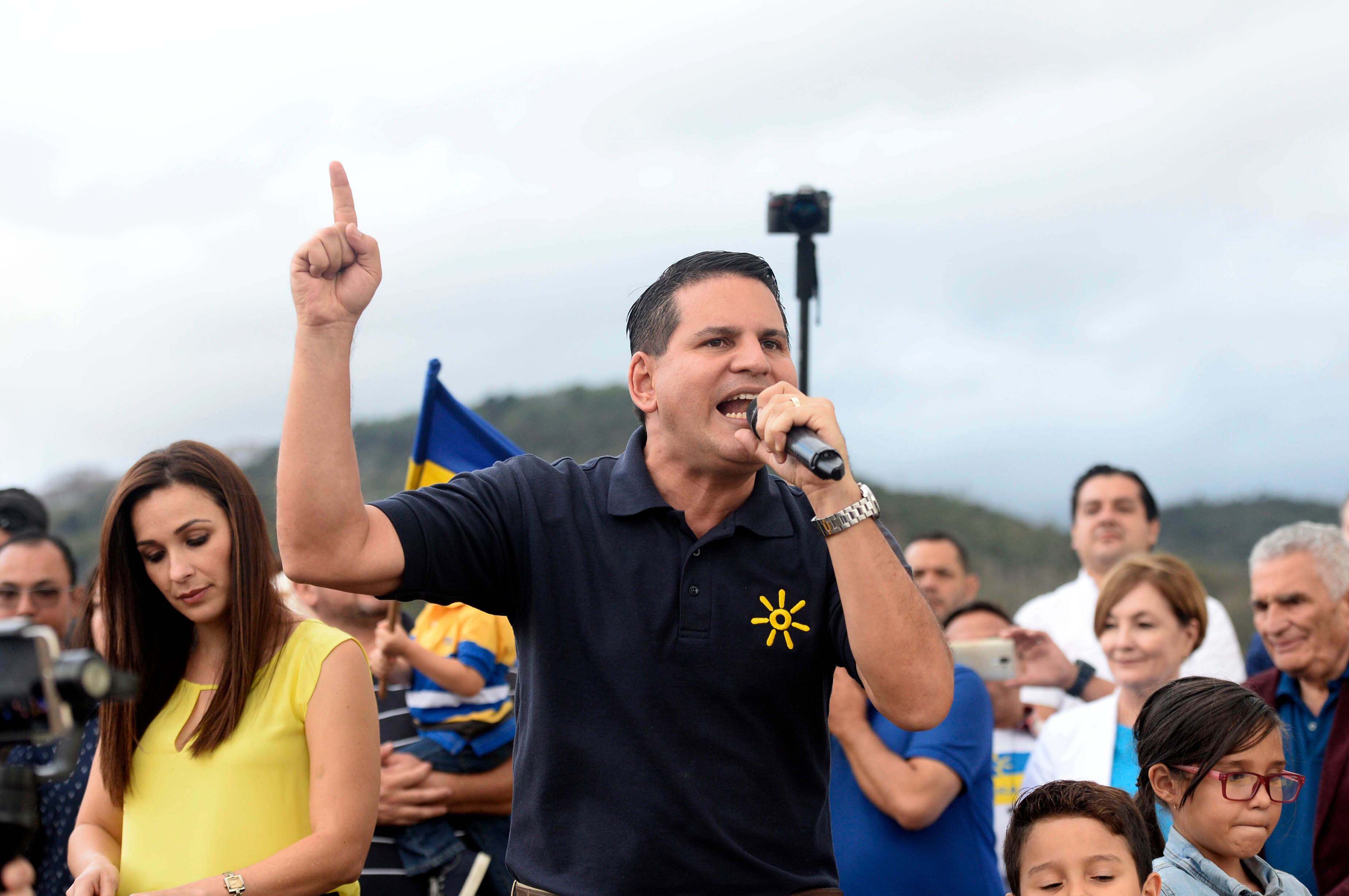Fabricio Alvarado, exdiputado y candidato presidencial del PRN, gesticula mientras sostiene un micrófono en un acto de campaña, acompañado de simpatizantes.