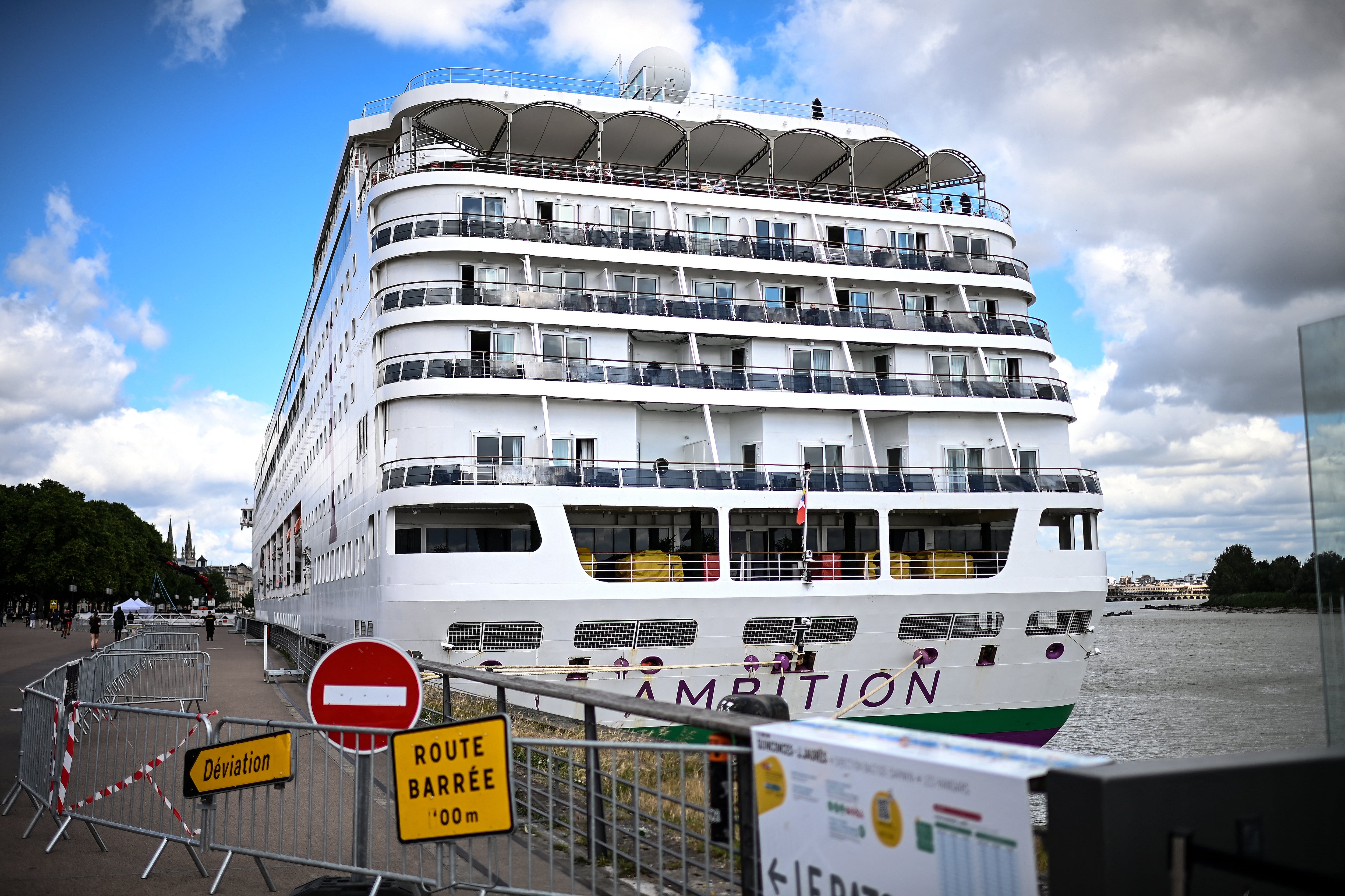 Pasajeros permanecen a bordo del crucero Ambition, con bandera de Bahamas, después de quedar confinados tras un brote de enfermedad gastrointestinal en la embarcación, en el puerto de Burdeos, en el suroeste de Francia, el 13 de mayo del 2026.
Las autoridades francesas confinaron el 13 de mayo a más de 1.700 pasajeros y tripulantes de un crucero británico atracado en Burdeos tras la muerte de un pasajero adulto mayor. Los funcionarios minimizaron cualquier vínculo con la alerta por hantavirus. (Foto de Christophe Archambault / AFP)
