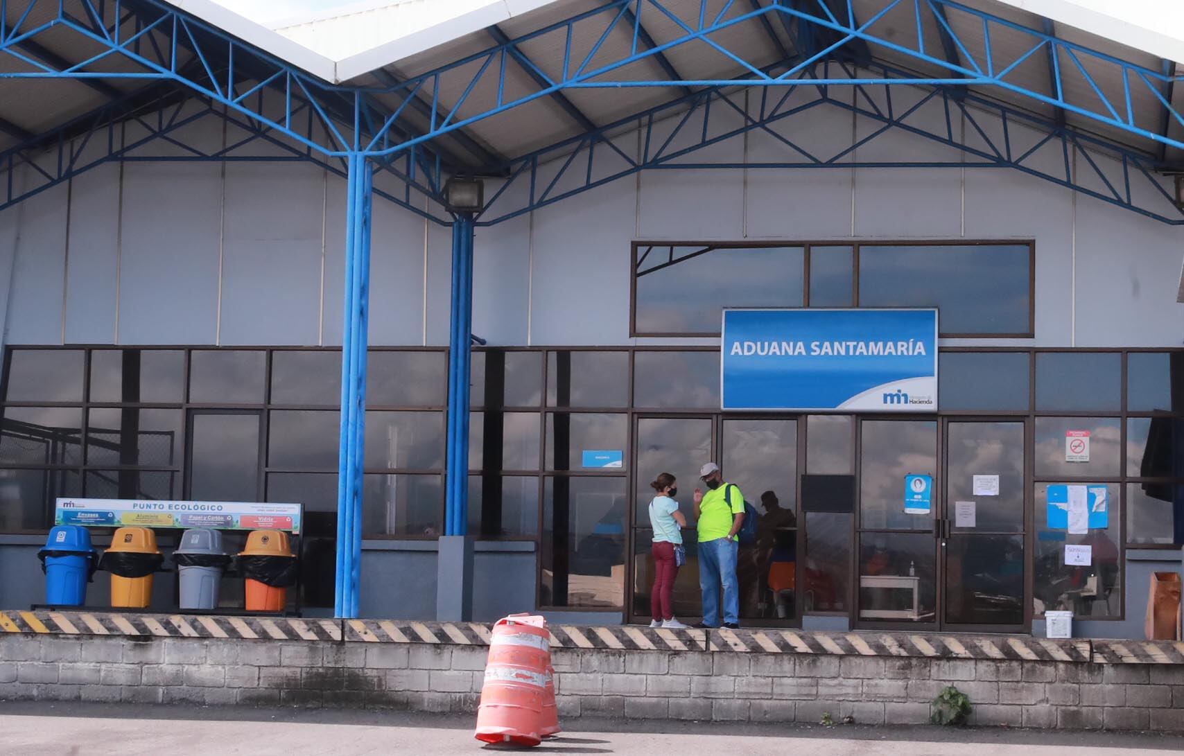 Fachada de la Aduana Santamaría en Costa Rica, con personas conversando en la entrada. Esta aduana forma parte del Ministerio de Hacienda, que ha reactivado la plataforma digital ‘Aduana Fácil’ para trámites aduaneros.