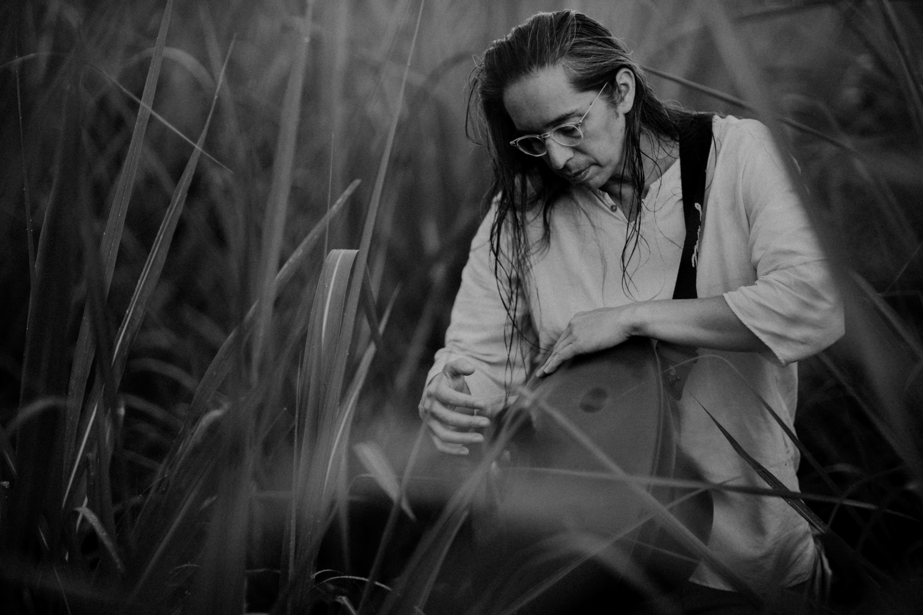 Imagen del músico costarricense Carlos 'Tapado' Vargas sosteniendo un tambor en medio de un escenario natural. Además de un perro de color blanco y negro y un gato de color café claro.