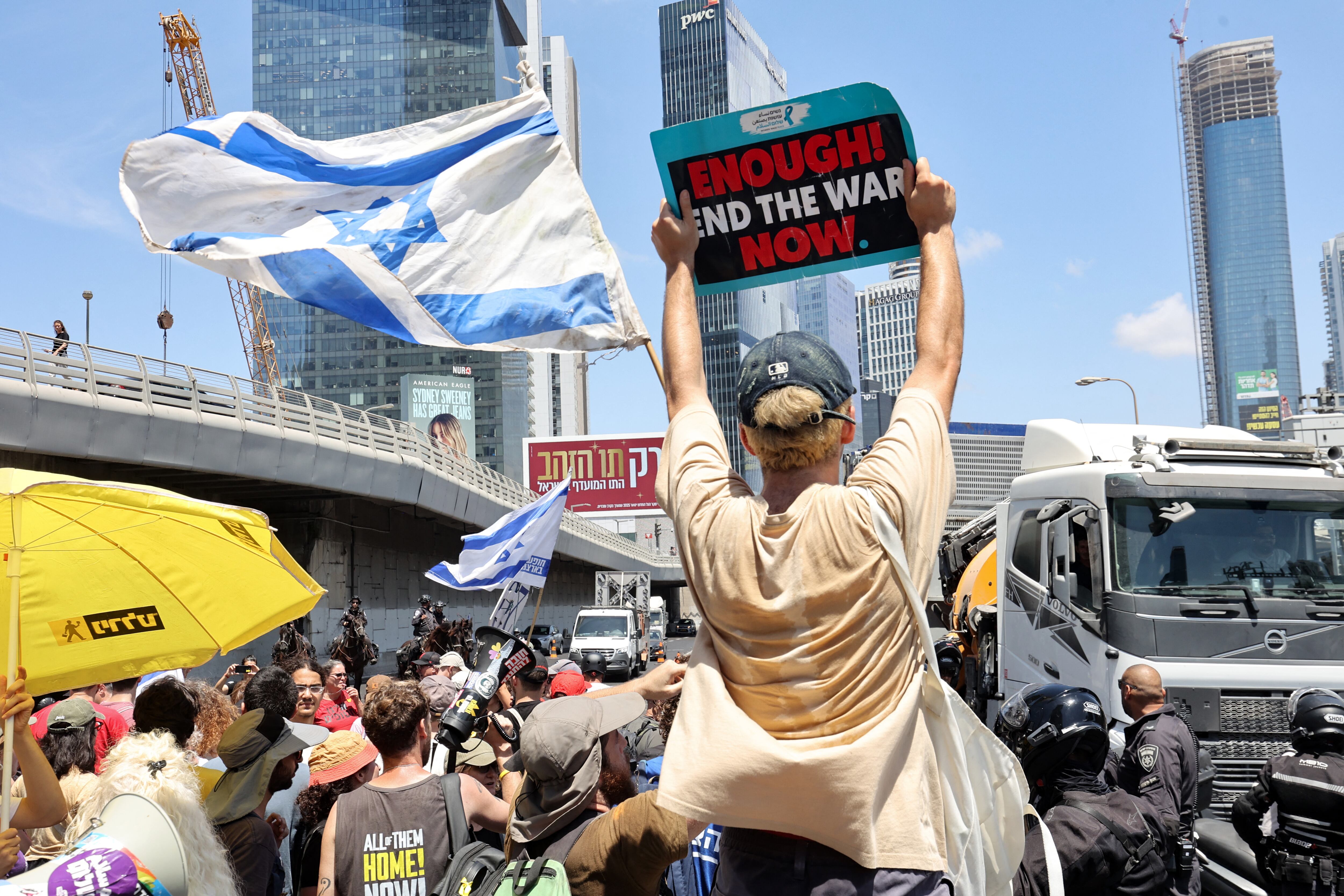 A demonstrator holds up a placard as others block a road during an anti-government protest demanding a deal to release Israelis detained in the Gaza Strip by Hamas militants since October 7, 2023, in Tel Aviv on August 17, 2025. Demonstrators took to the streets across Israel on August 17, 2025, more than a week after Israel's security cabinet approved plans to capture Gaza City and nearby camps, following 22 months of war that have created dire humanitarian conditions. (Photo by GIL COHEN-MAGEN / AFP)
