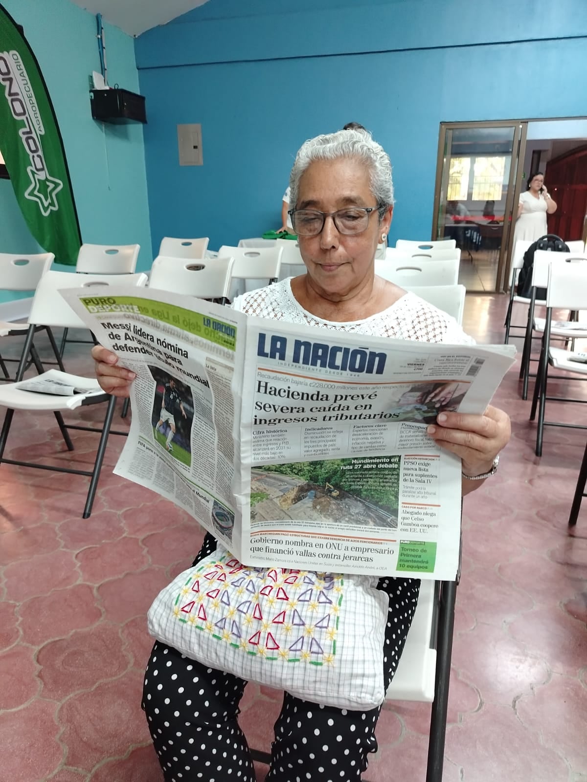 Una mujer lee el periódico La Nación sentada en una silla.