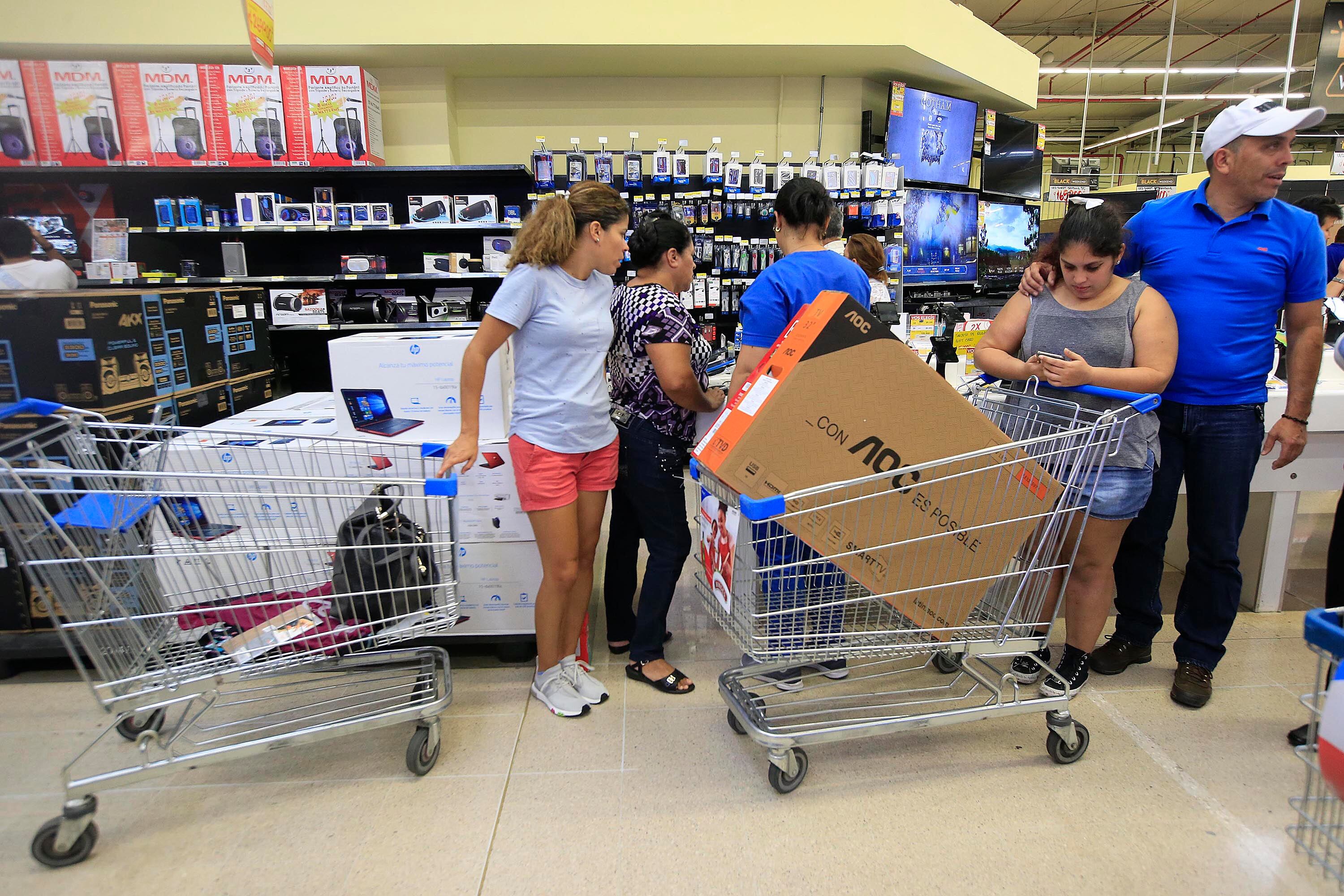 Personas comprando televisores y productos electrónicos con descuentos en una tienda durante el Black Friday en Costa Rica, con carritos de compra llenos.